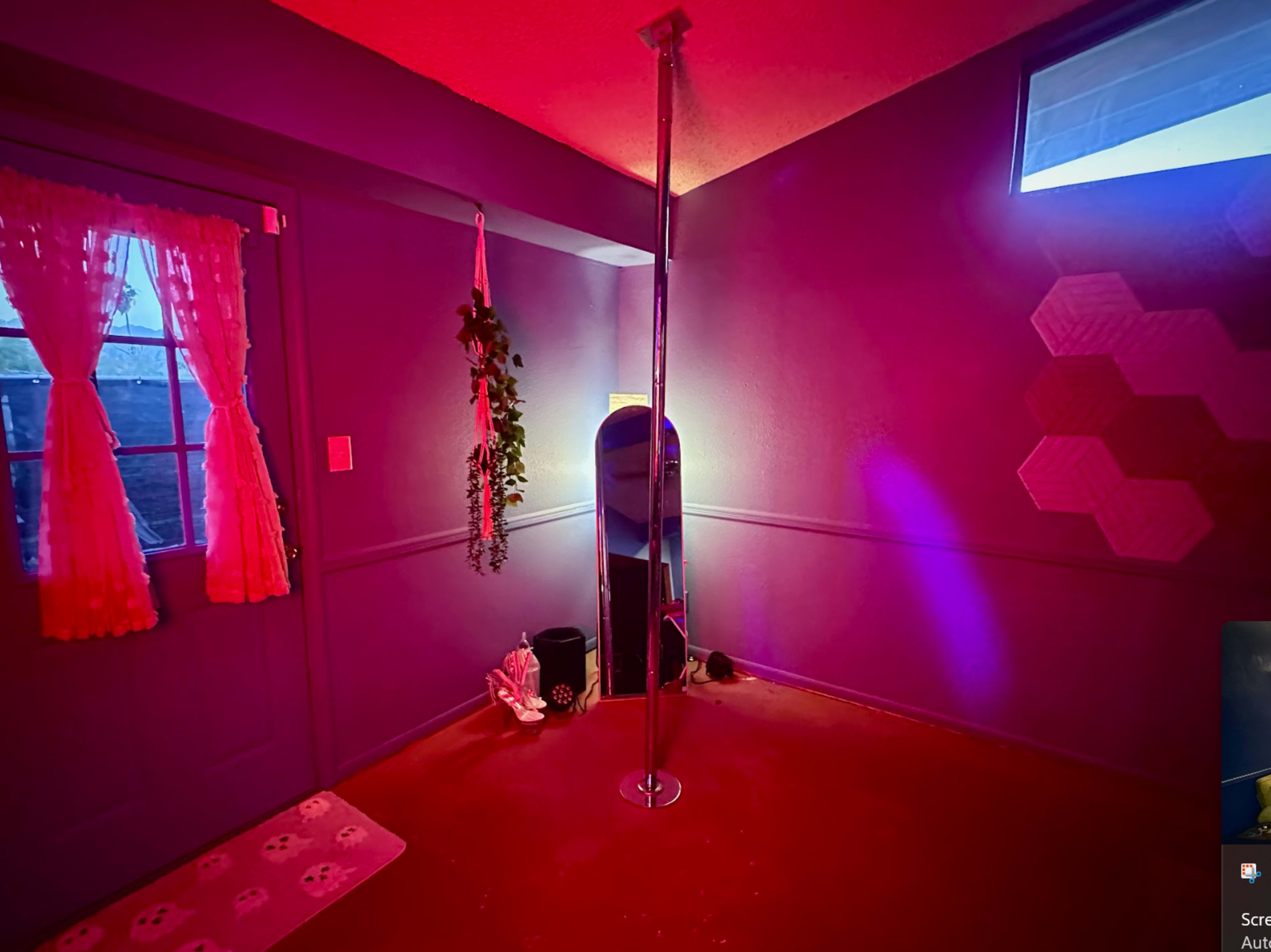 The room features a metallic pole in the corner, surrounded by colored lighting, with a door and a mirror visible along the walls.