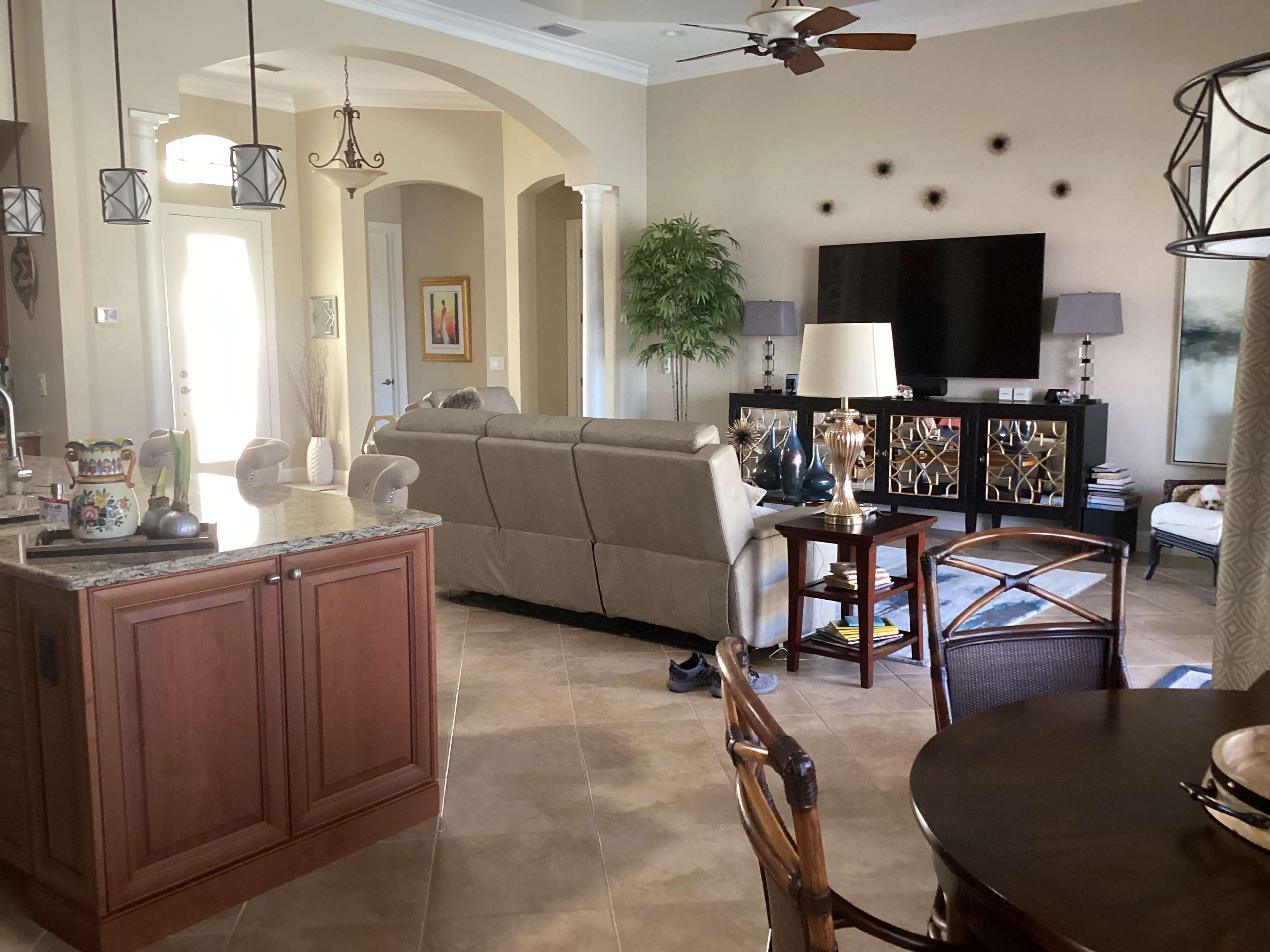 A spacious living area with a kitchen counter, a beige sofa facing a television, and a dining table with wicker chairs.