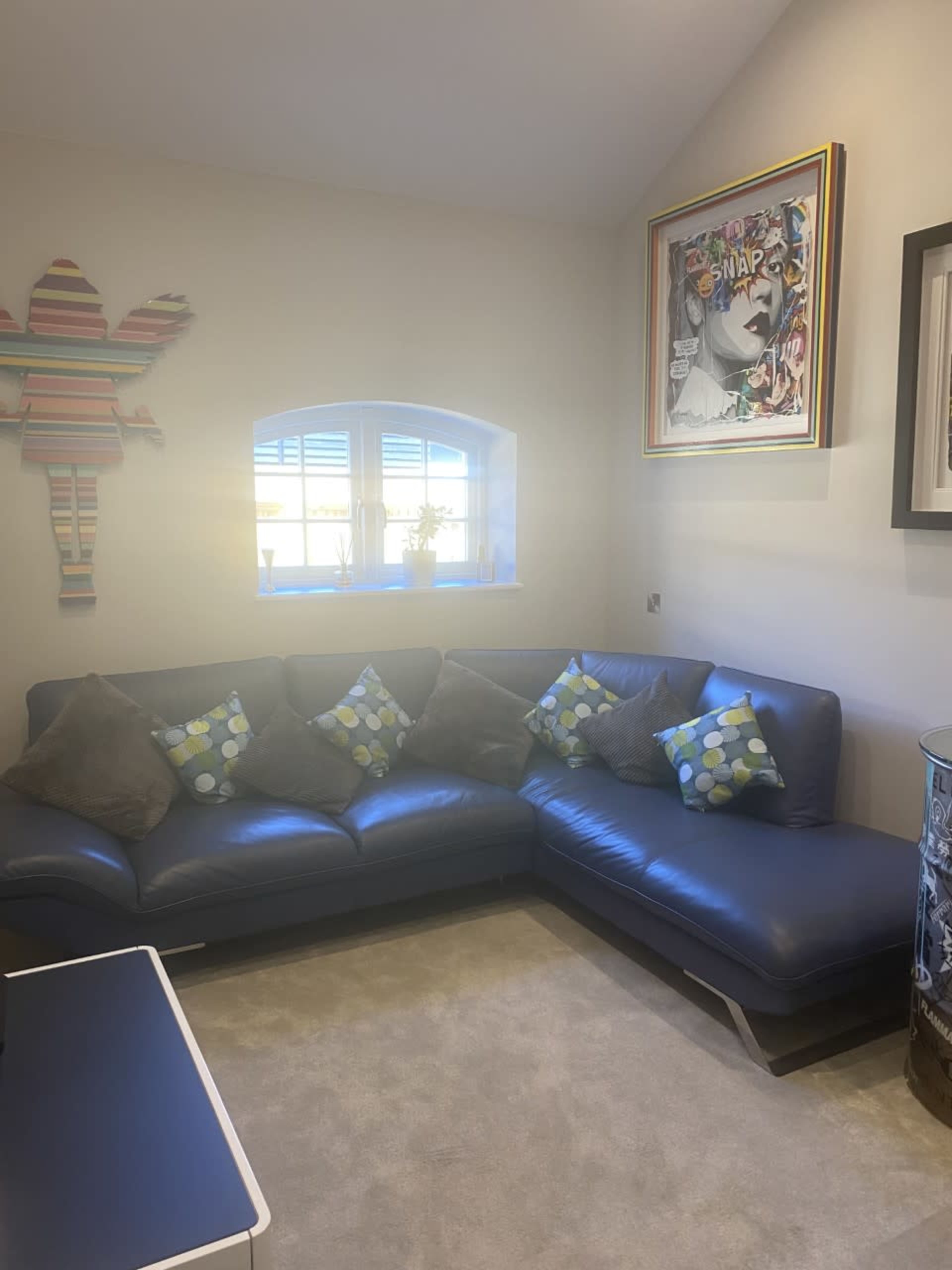 A corner of a living room with a navy blue sectional sofa adorned with polka dot pillows, a wall art piece, and a decorative figure on the wall.