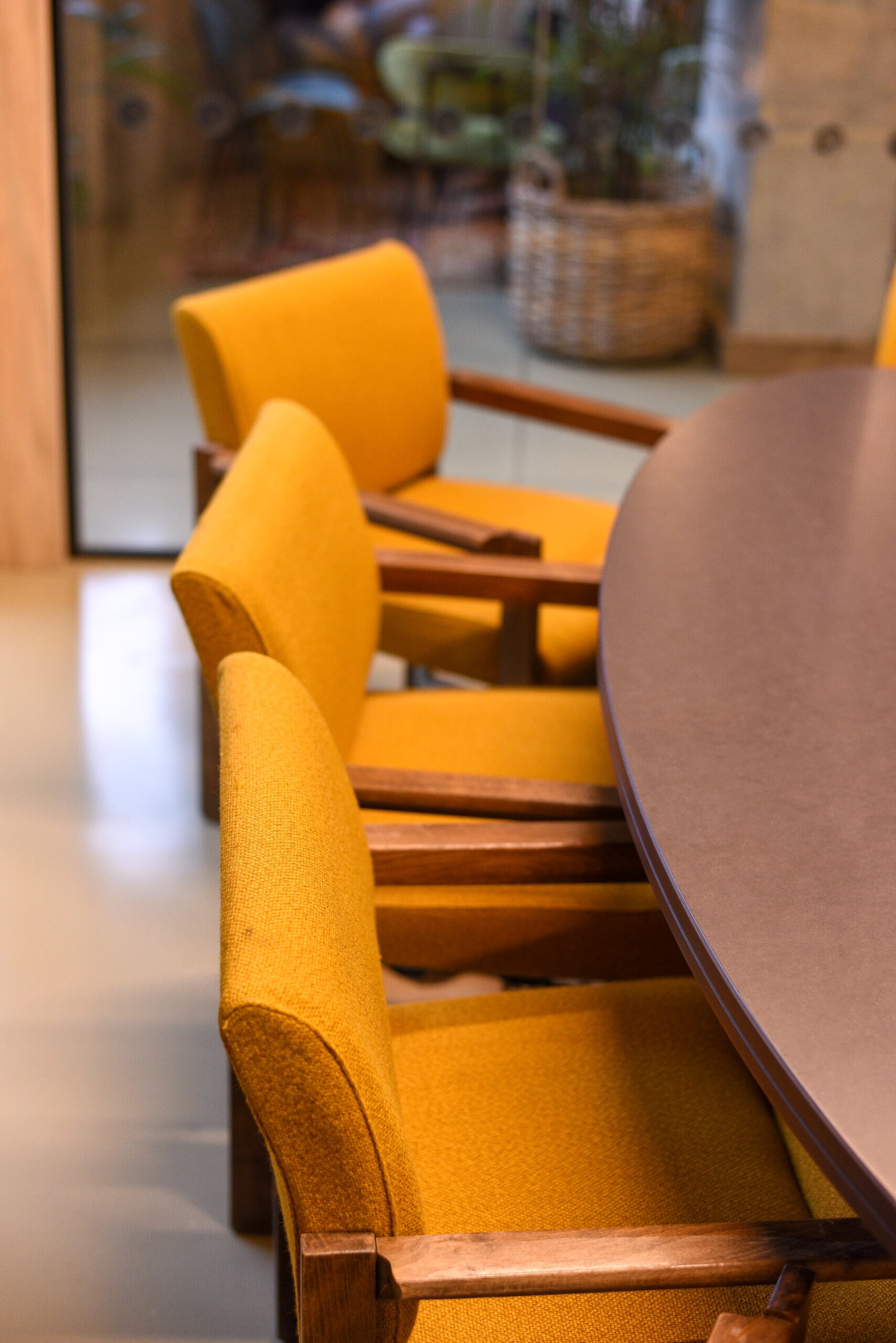 The image shows a round table accompanied by several yellow upholstered chairs with wooden armrests.