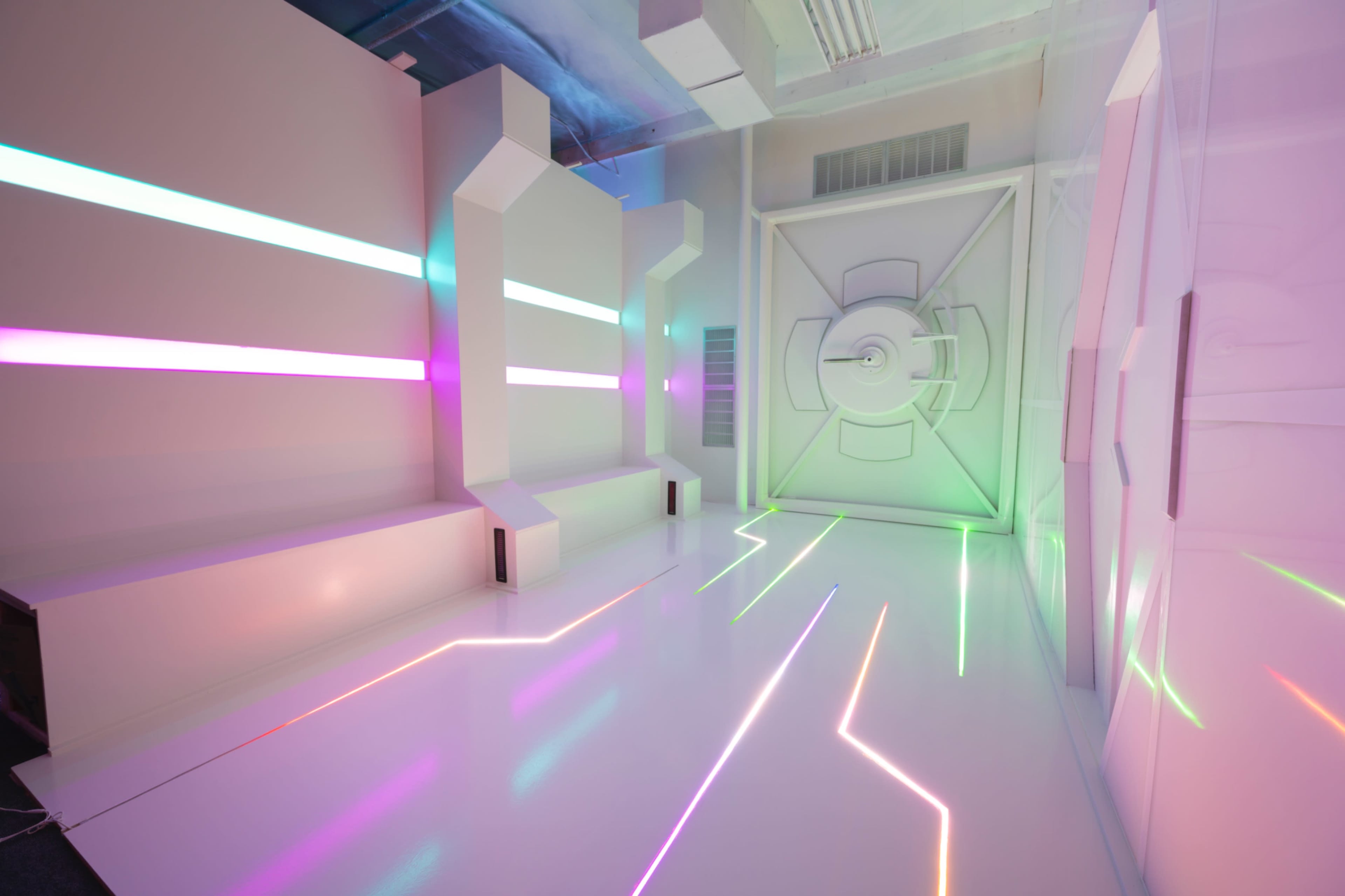 A modern, brightly lit room with white walls and colorful, neon stripes of light along the surfaces and floor.