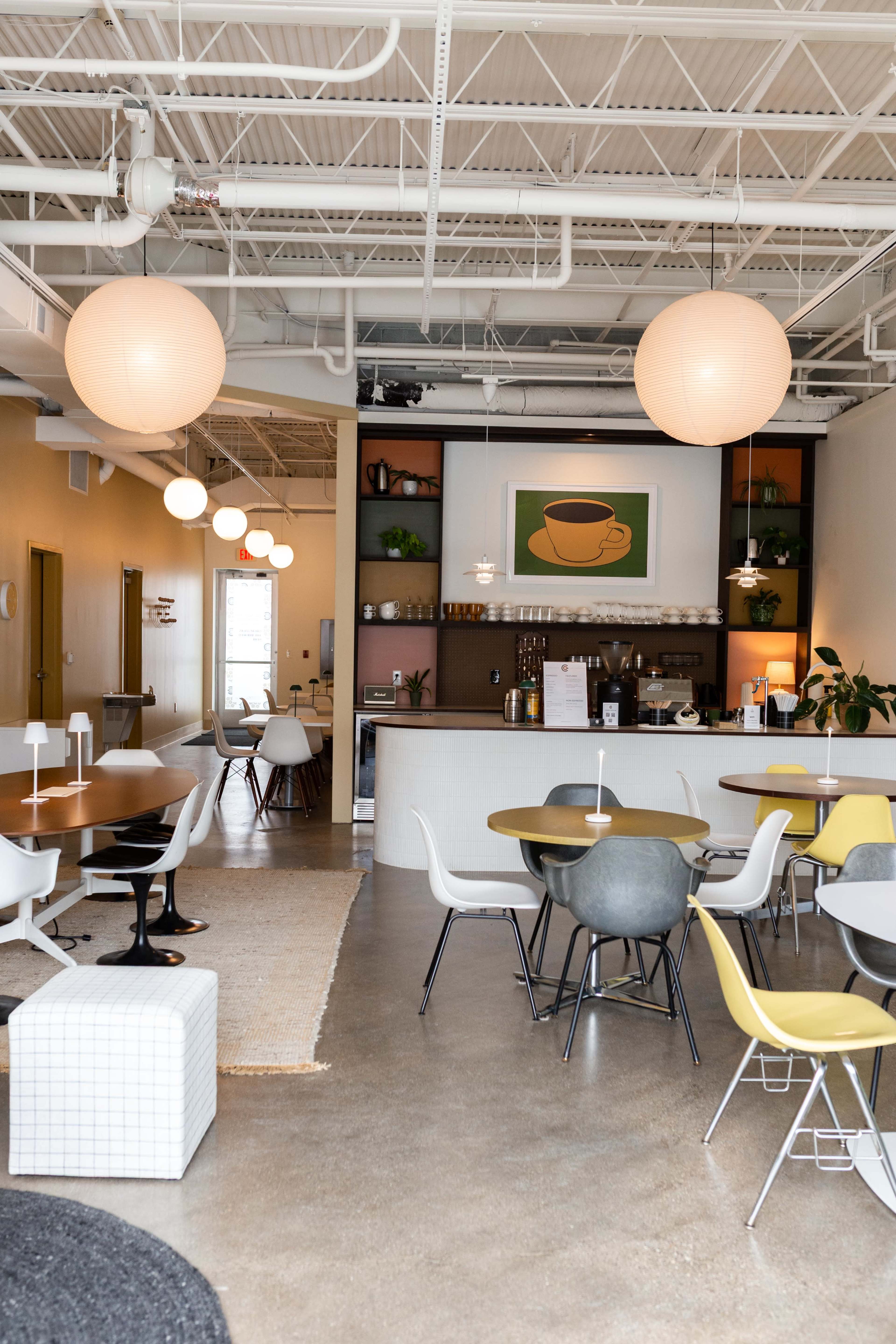 The image shows a modern café interior with a mix of seating arrangements, decorative wall shelves, and pendant lighting.
