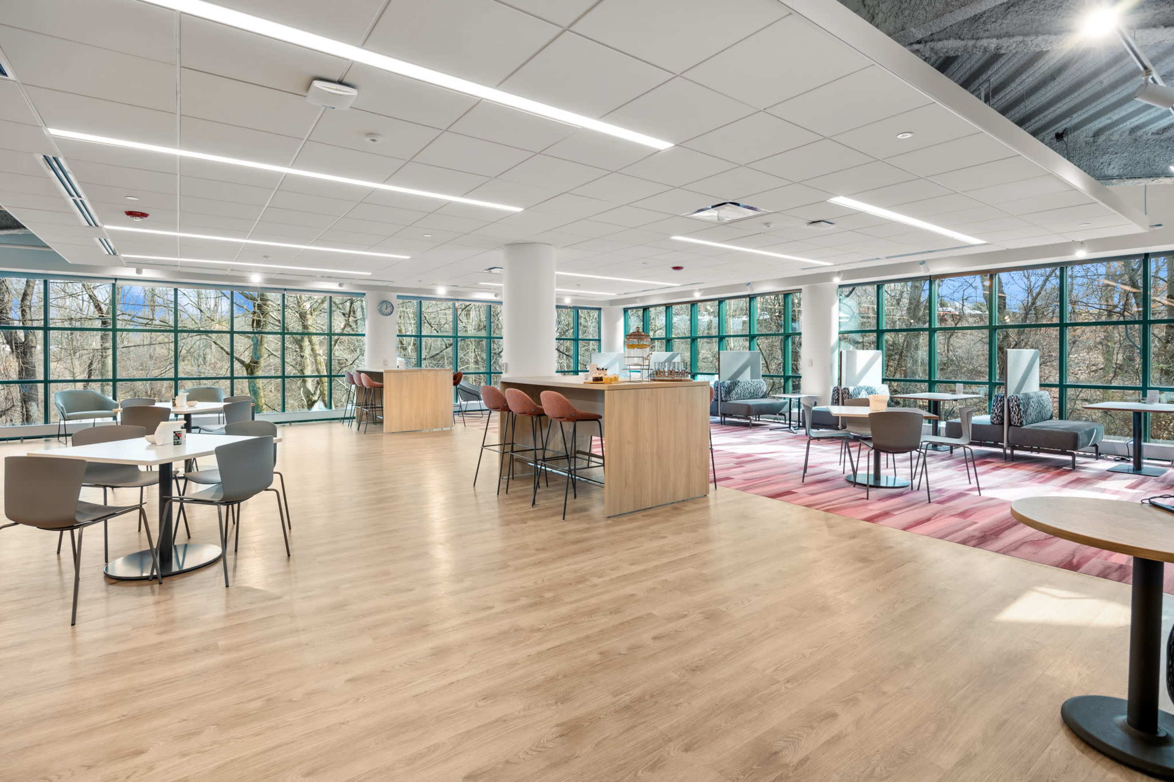 A spacious, modern room features large windows with natural light, an open seating area with tables and chairs, and a central bar area.