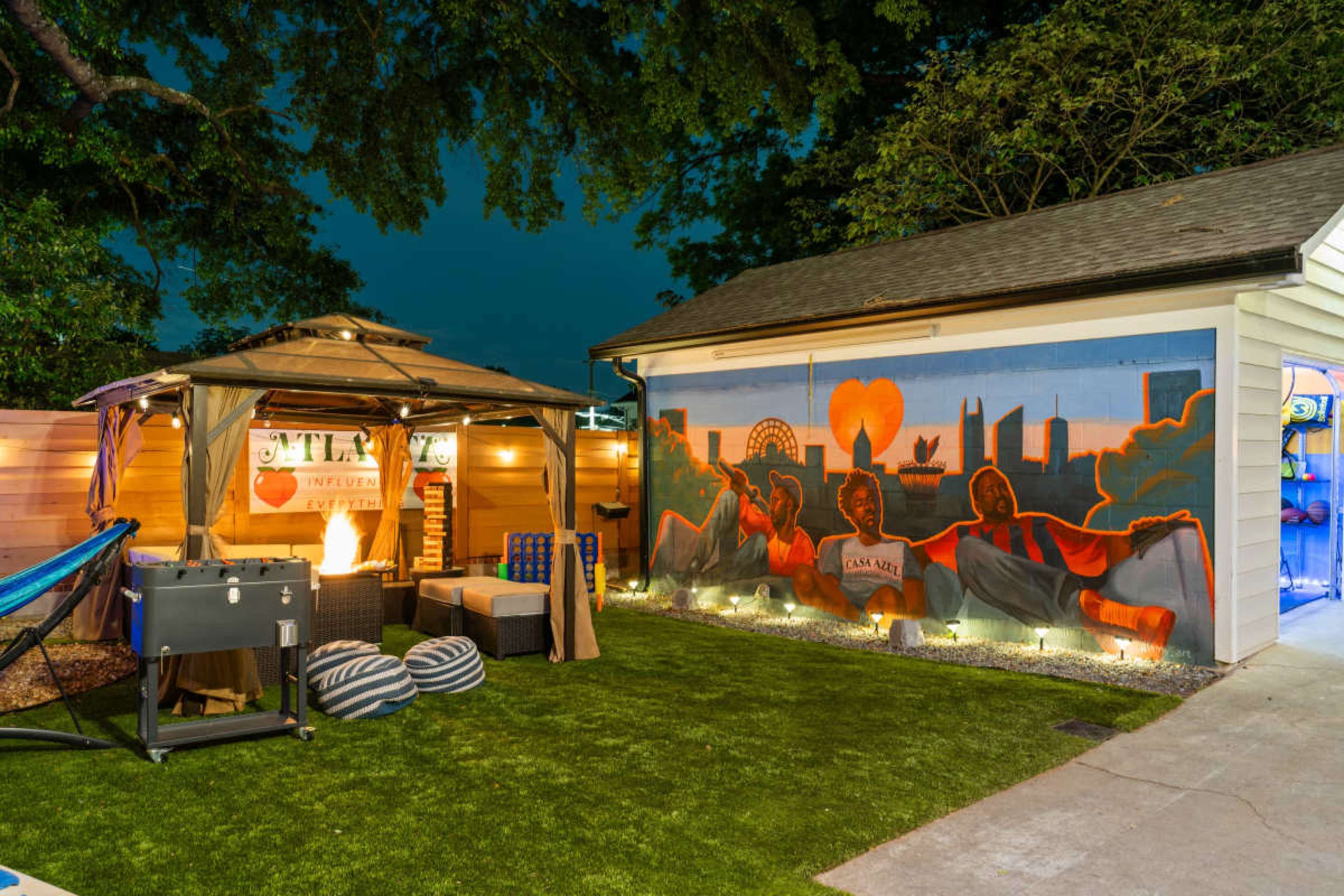 The image shows a backyard scene featuring a gazebo, outdoor seating area, and a colorful mural on a nearby wall.