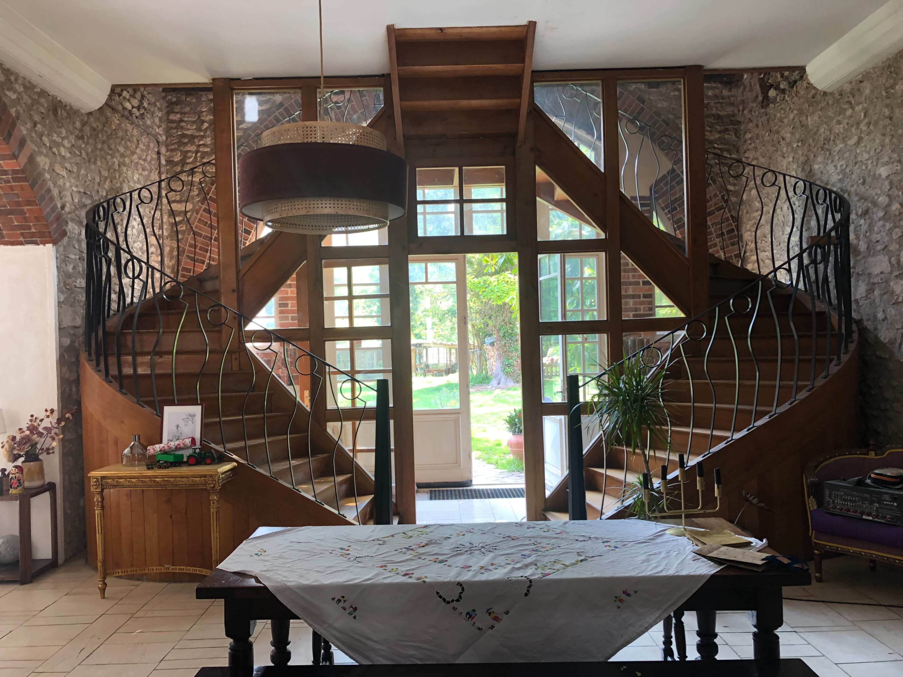 An interior entrance featuring a wooden staircase with intricate railings, flanked by large windows that illuminate the space.