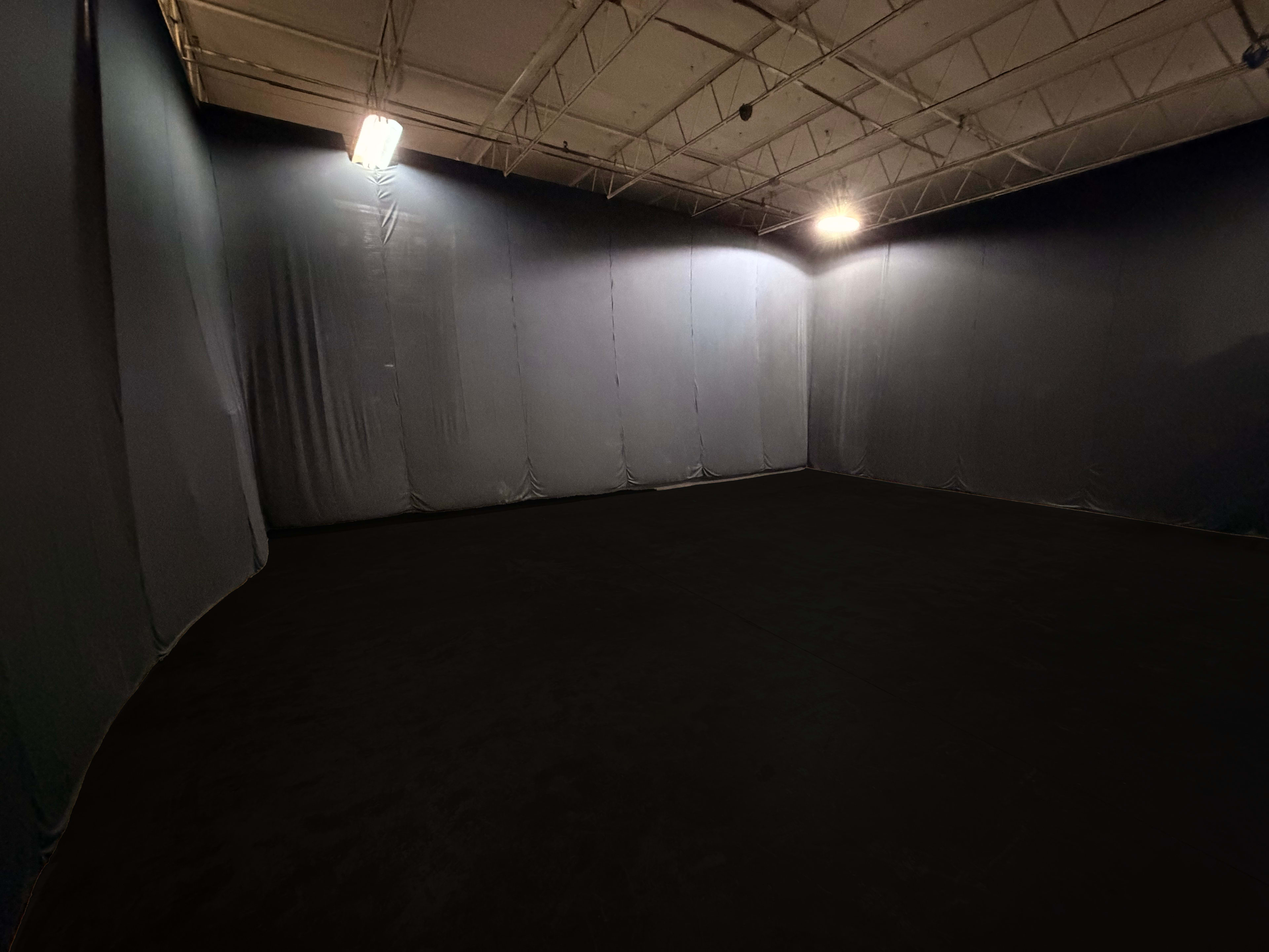 The image shows an empty room with black walls and a dark floor, illuminated by overhead lights.