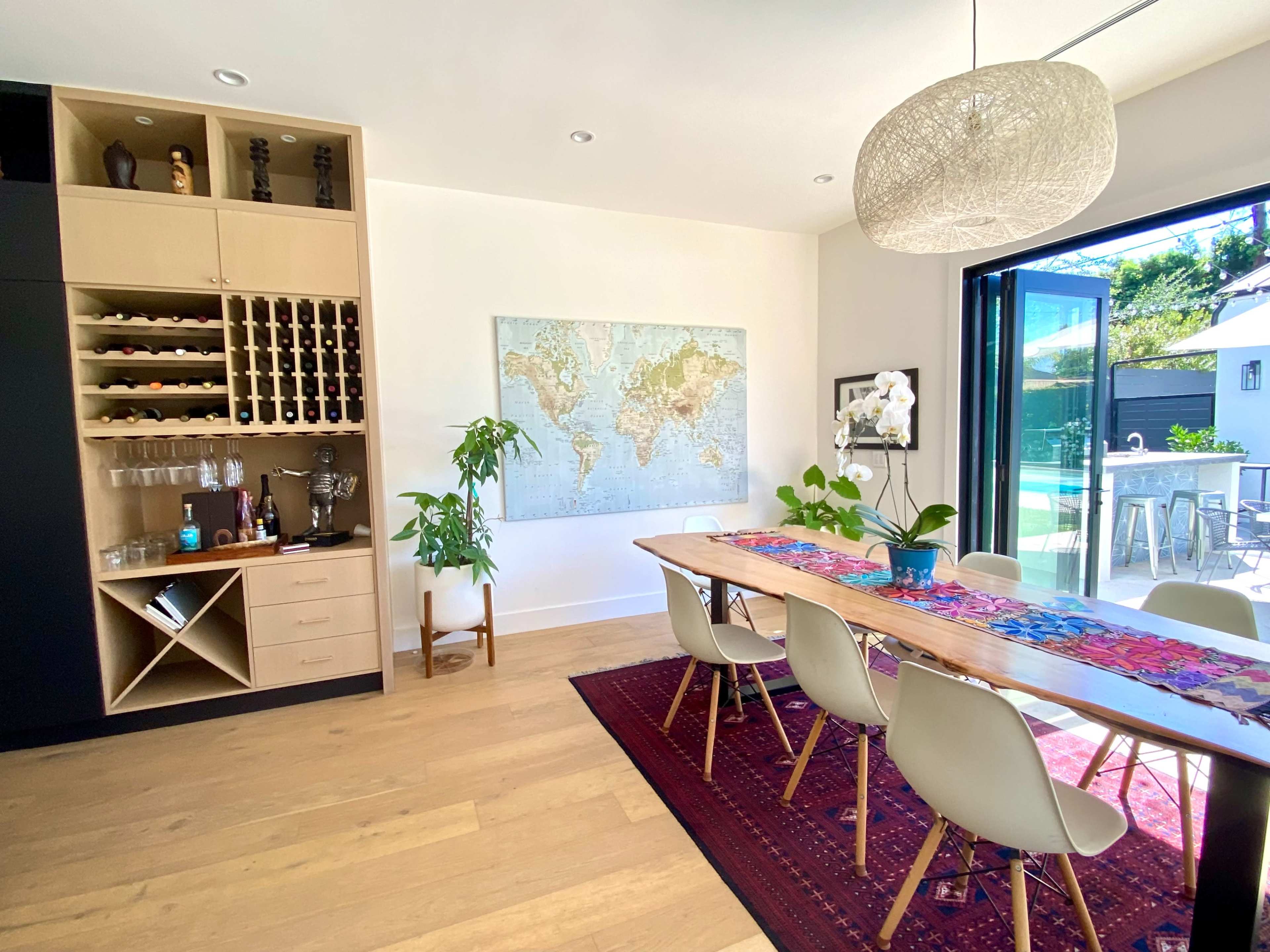 The dining area features a large wooden table surrounded by white chairs, with a world map hanging on the wall and a cabinet filled with decorative items and glassware.