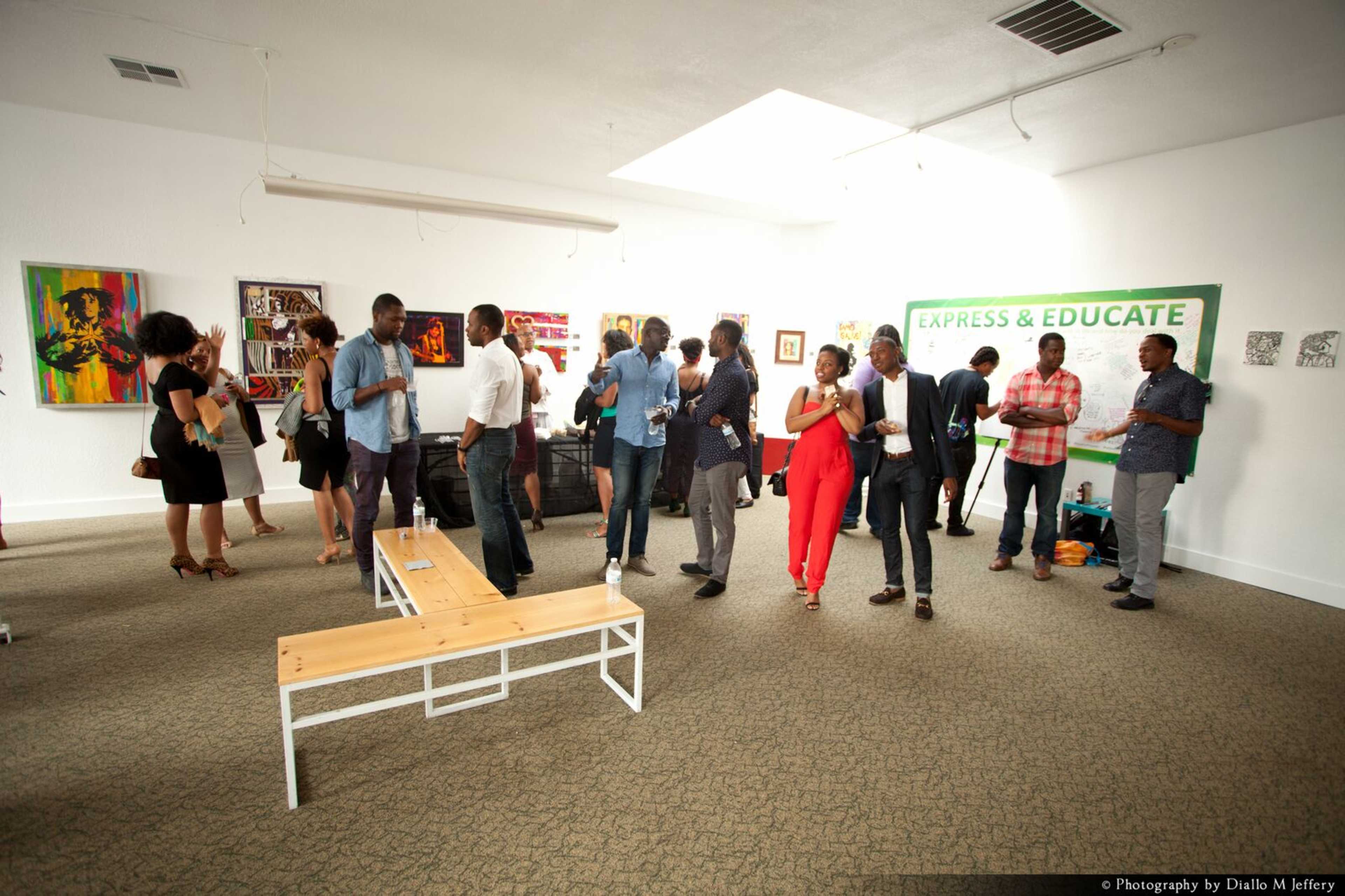 People socialize at an art gallery event featuring various artworks on the walls.