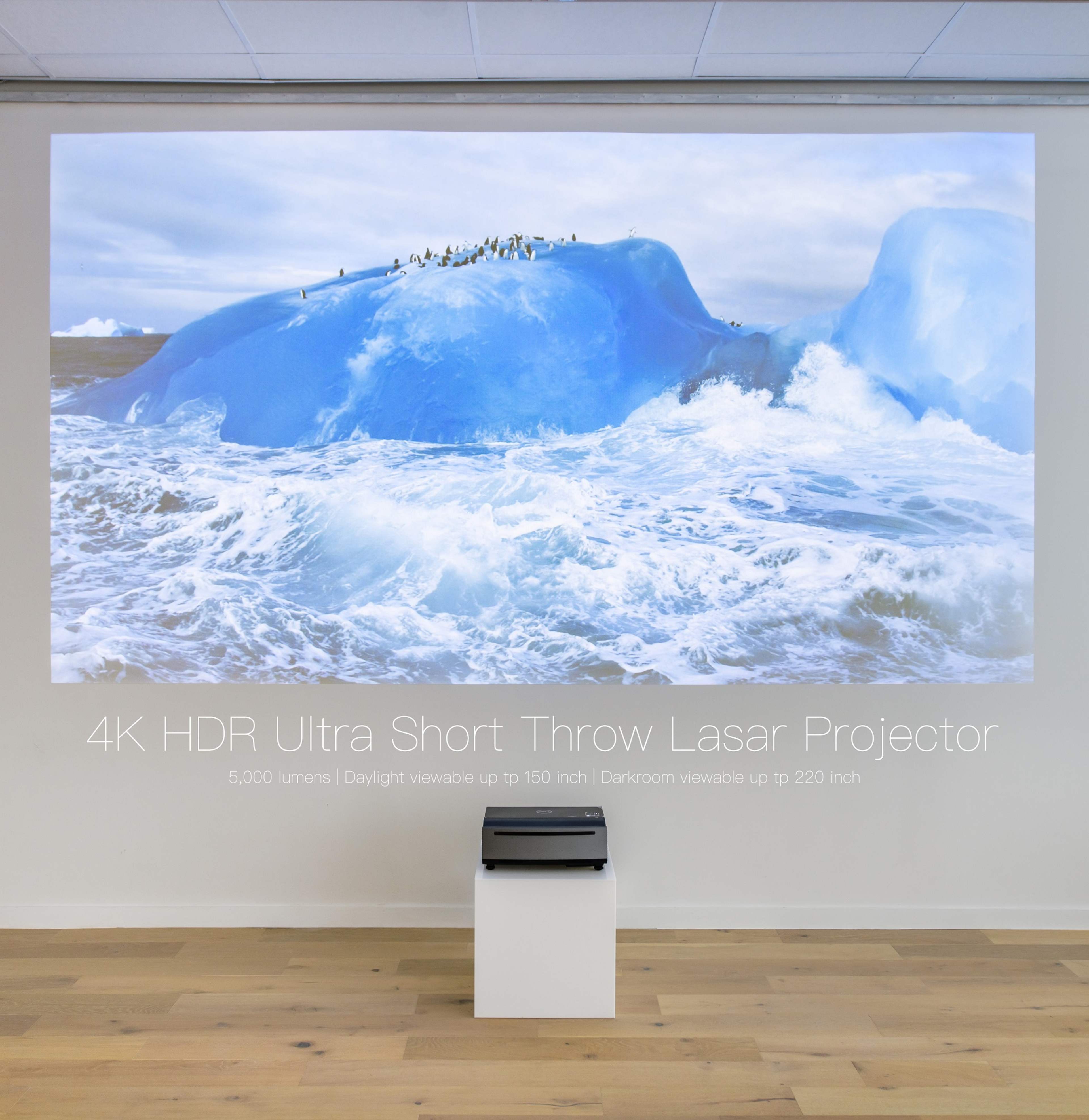 A 4K HDR ultra short throw laser projector displays an image of a blue iceberg surrounded by ocean waves on a large wall.