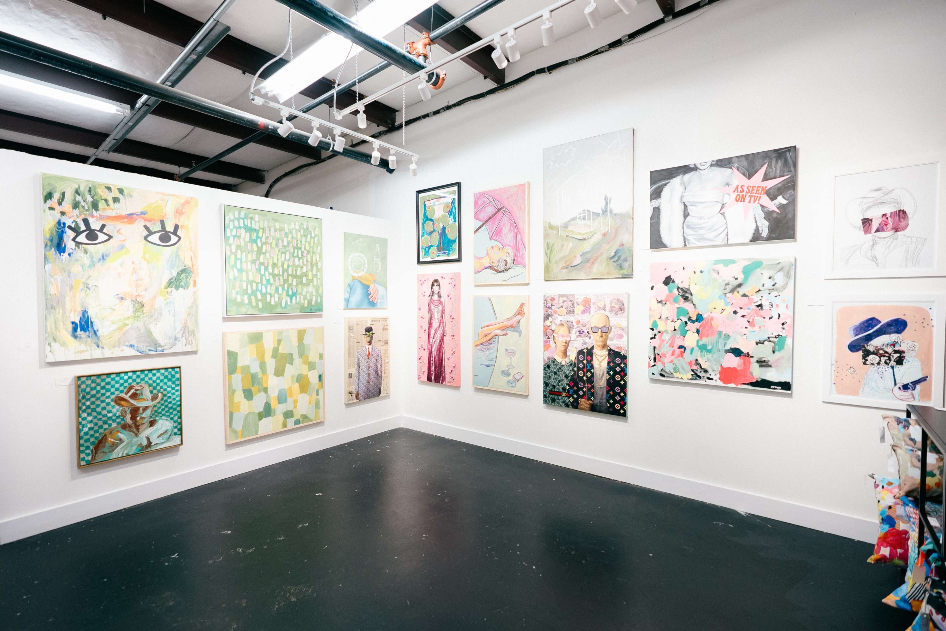 The image shows an art gallery wall featuring a variety of colorful paintings arranged in a grid pattern.