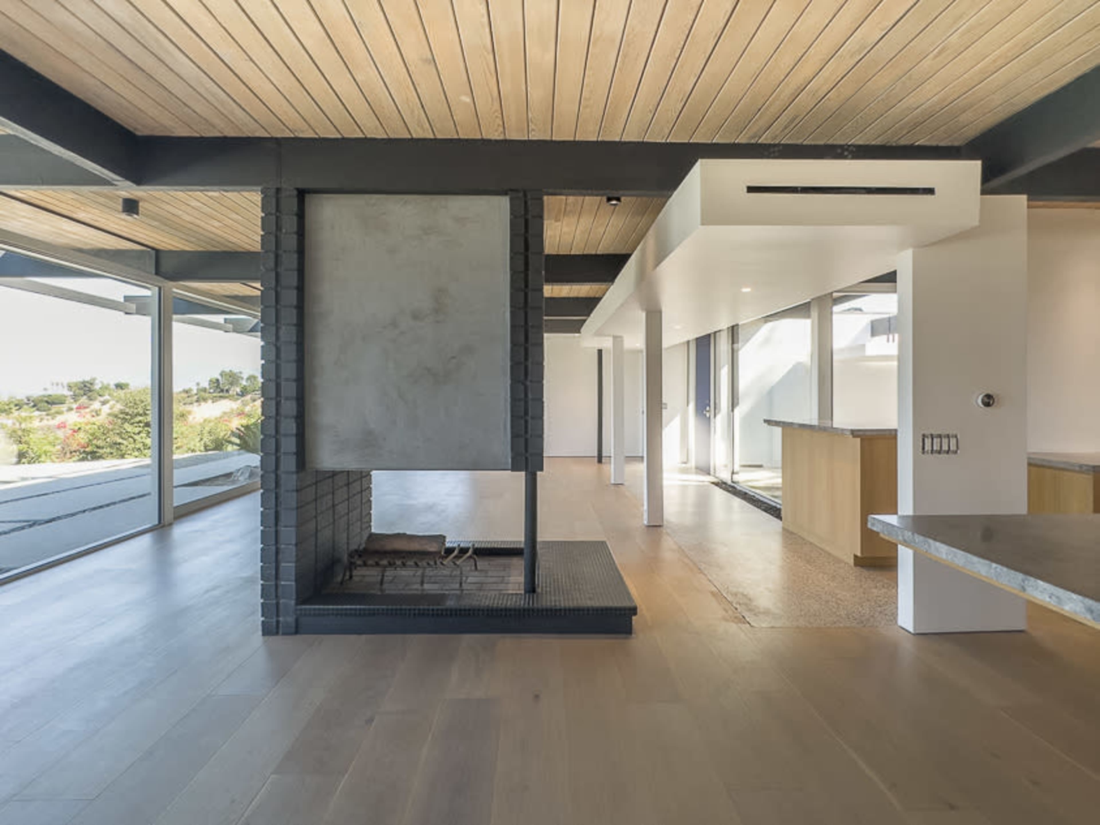 A modern interior space featuring a central fireplace, wooden ceilings, and large windows that allow natural light to enter.
