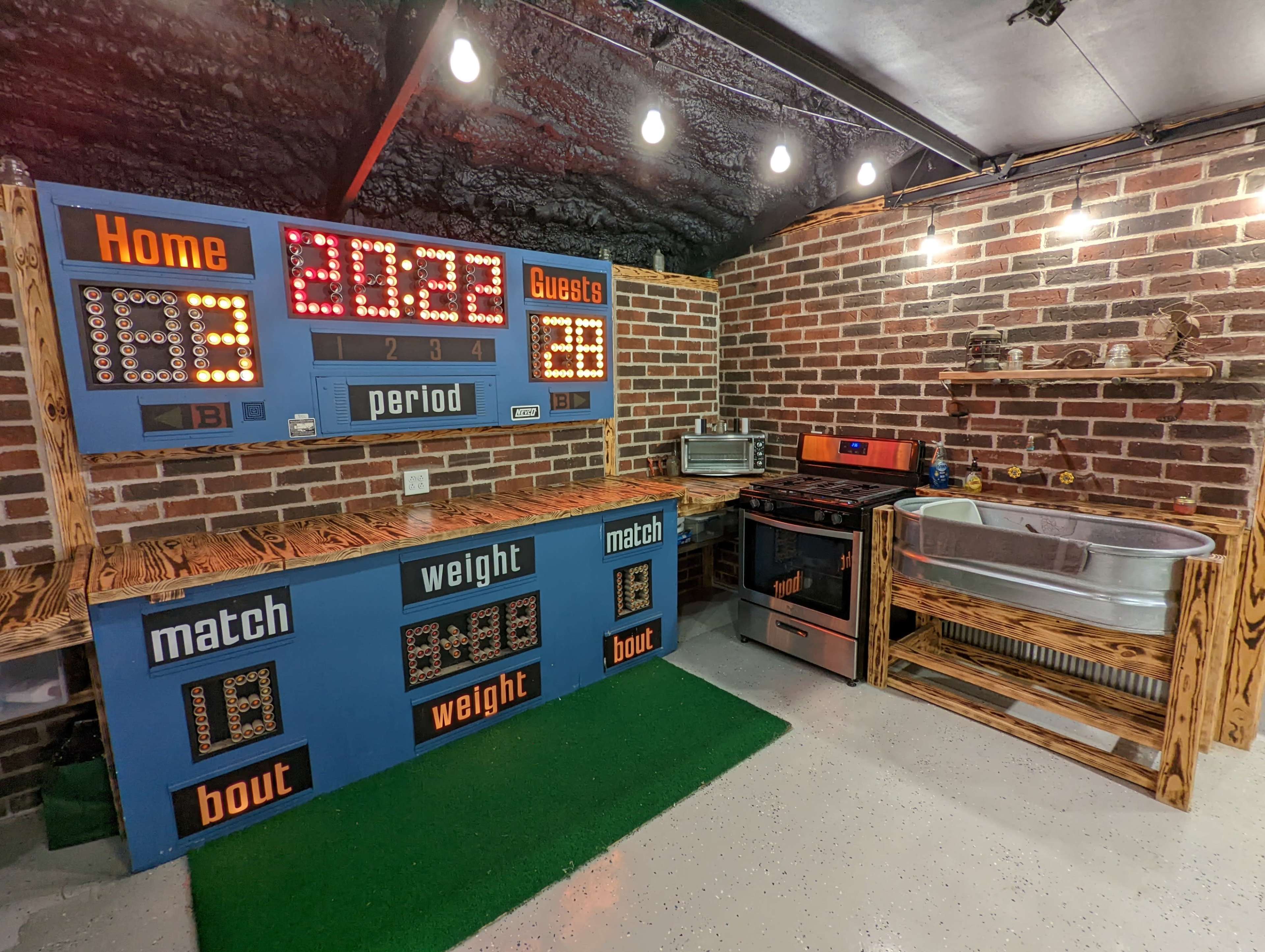 The image shows a brick-walled game room featuring a large scoreboard labeled "Home" and "Guests," with a retro cooking area that includes an oven, sink, and various kitchen items.