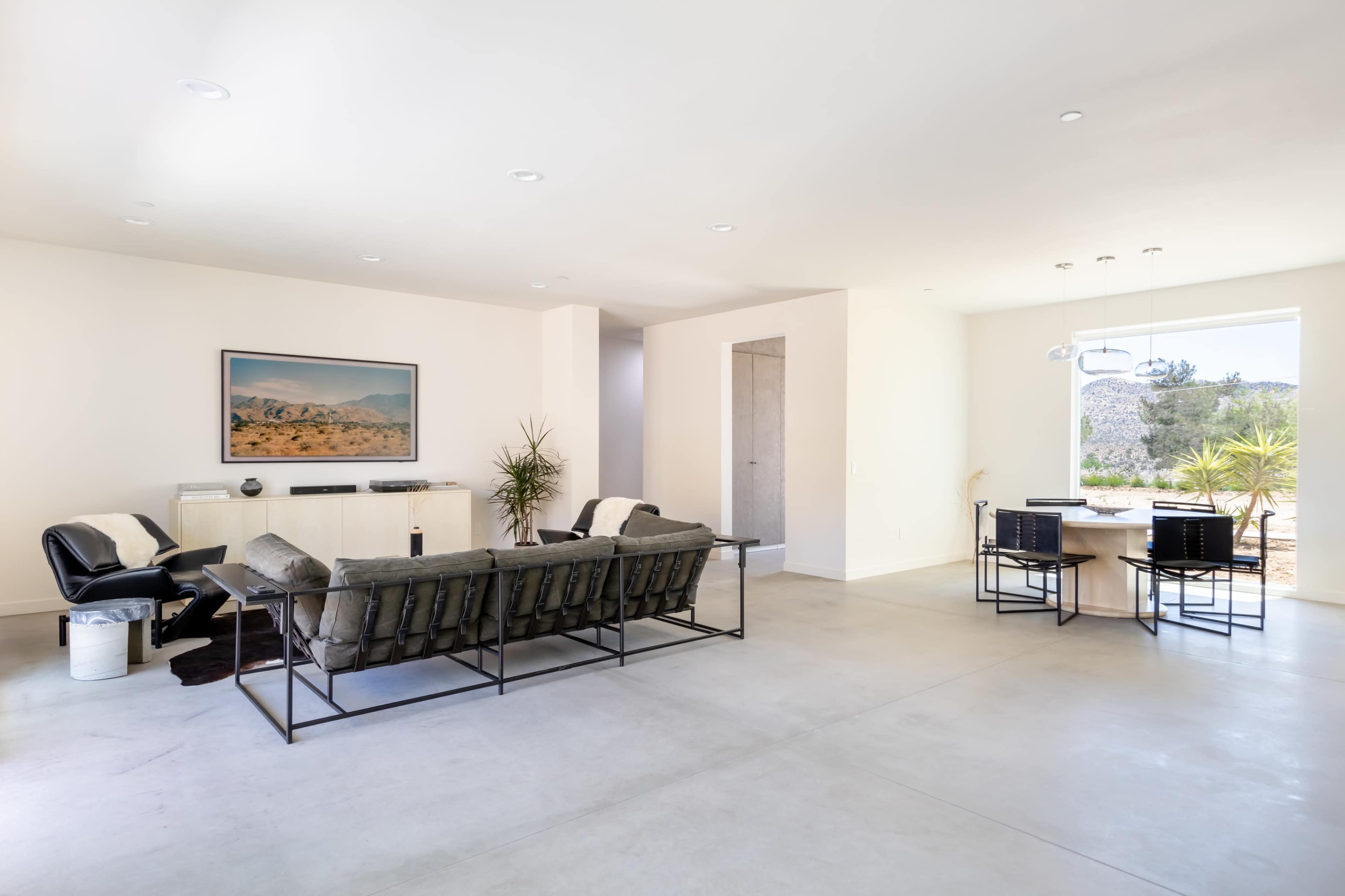 A modern living room with minimalist furniture, a large window, and a dining area adjacent to it.