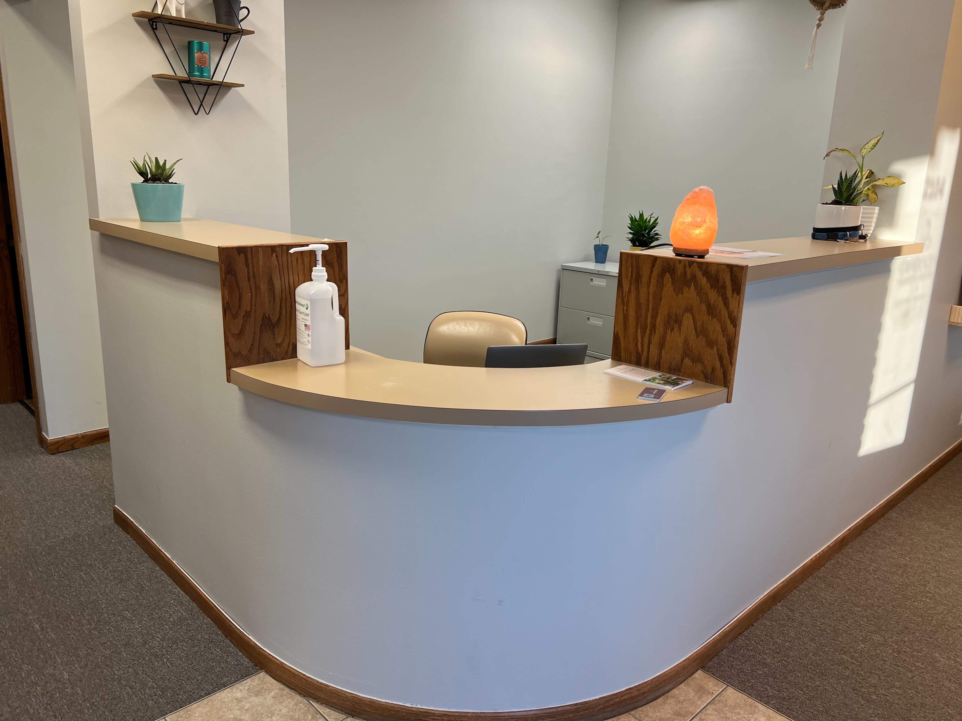 A reception area with a curved counter, a chair, potted plants, and a decorative lamp.