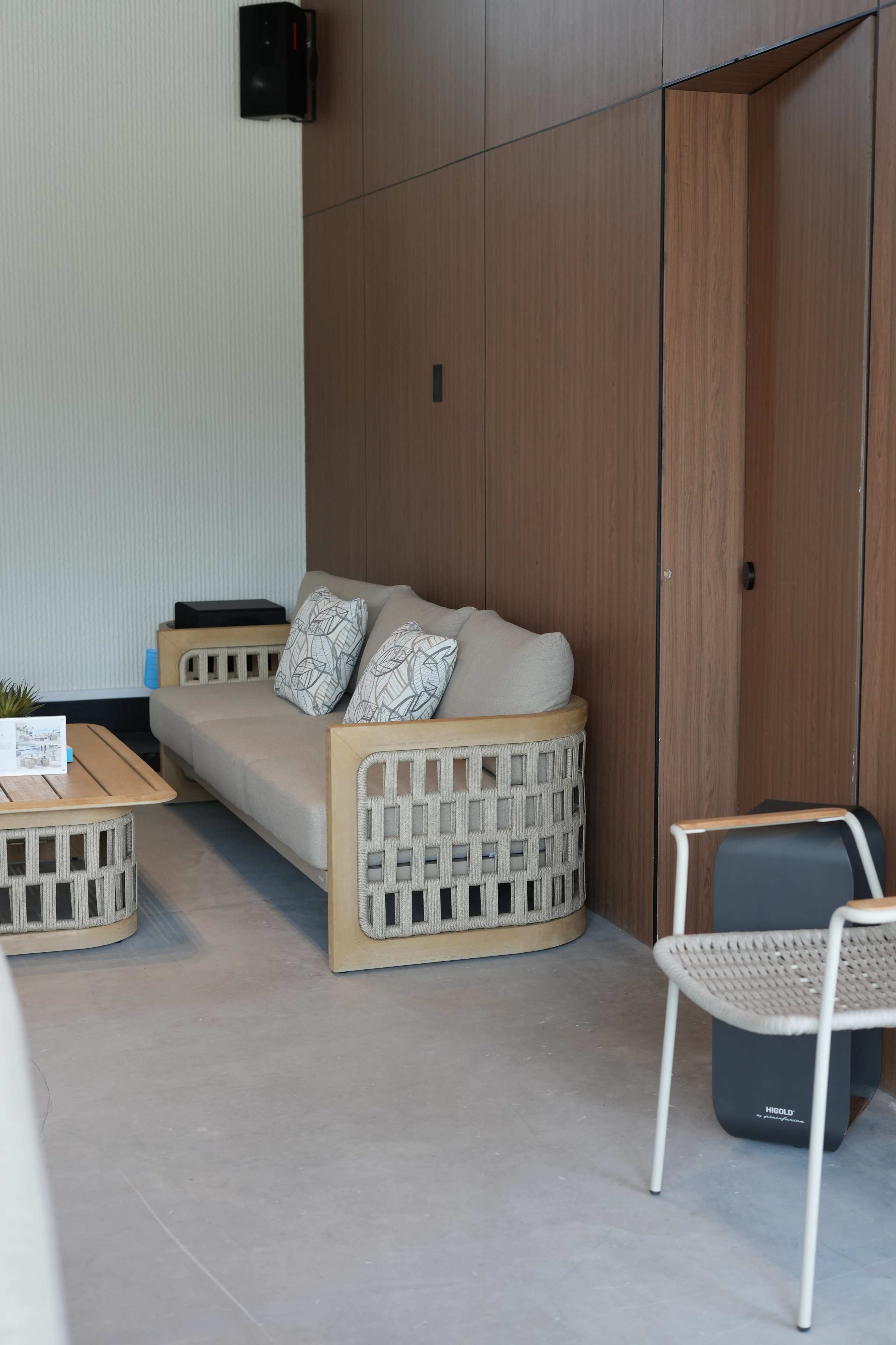 The scene shows a modern living area with a beige sofa adorned with patterned cushions, a wooden table, and a nearby door set within wooden paneling.