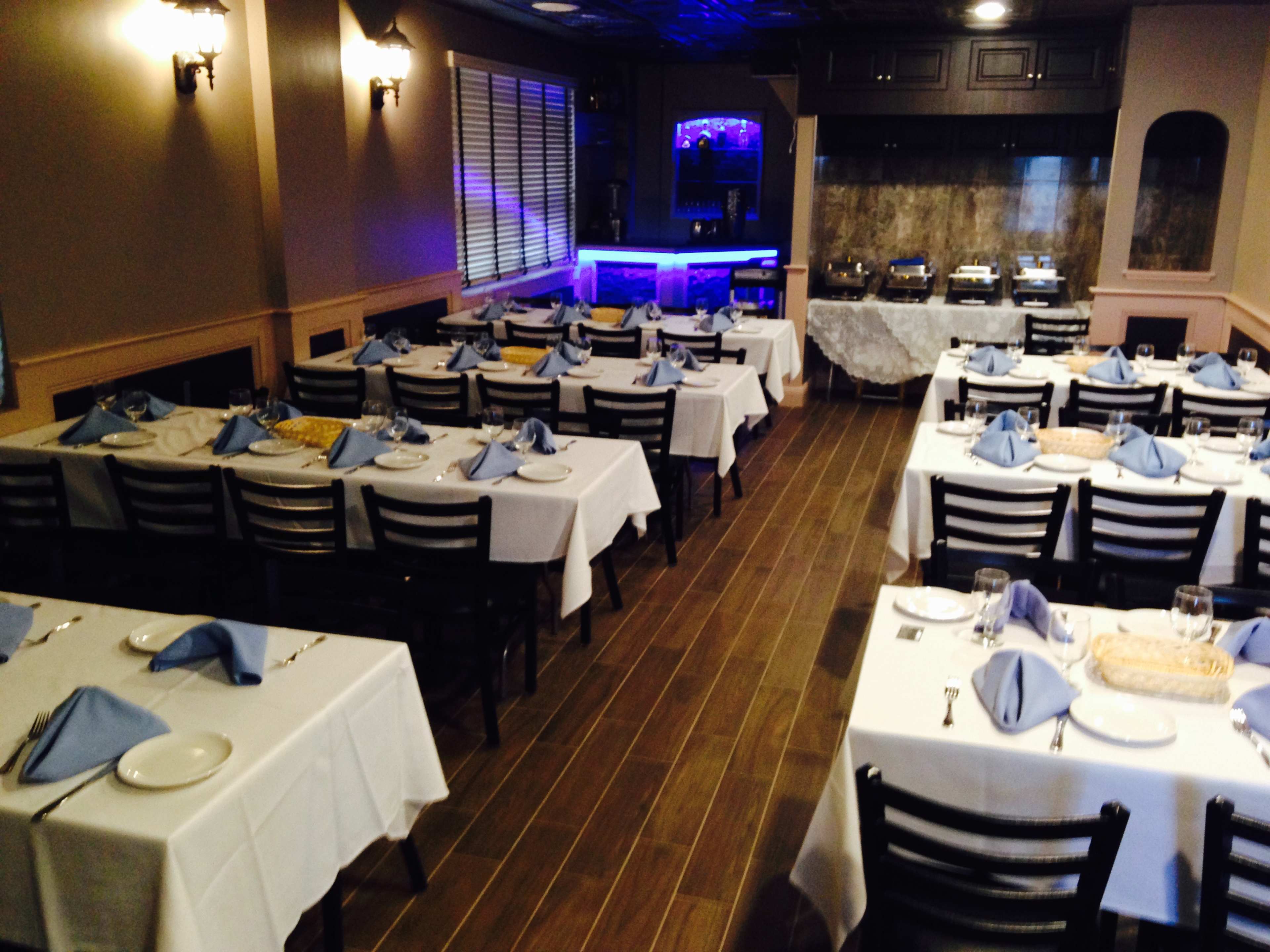 A dining area with neatly arranged tables covered in white tablecloths and blue napkins, along with a buffet station in the background.
