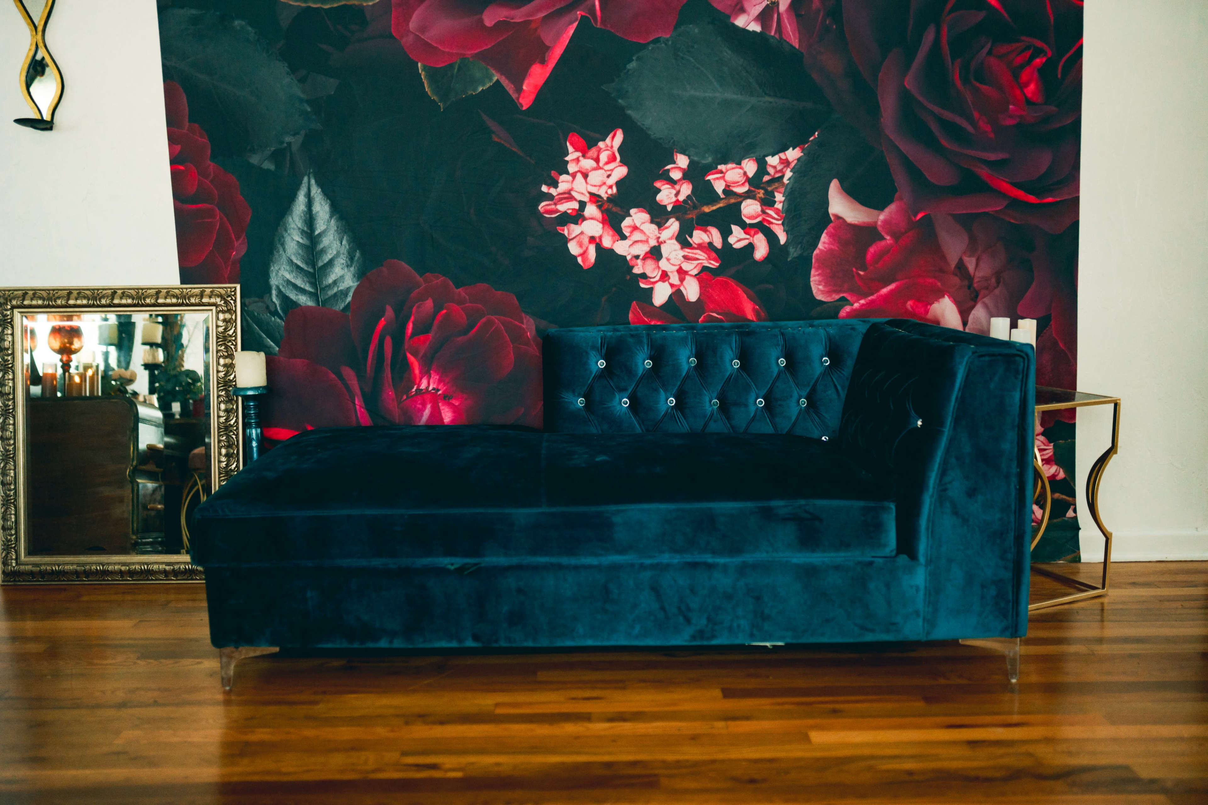 A plush blue chaise lounge is placed against a floral wallpaper featuring large red roses.