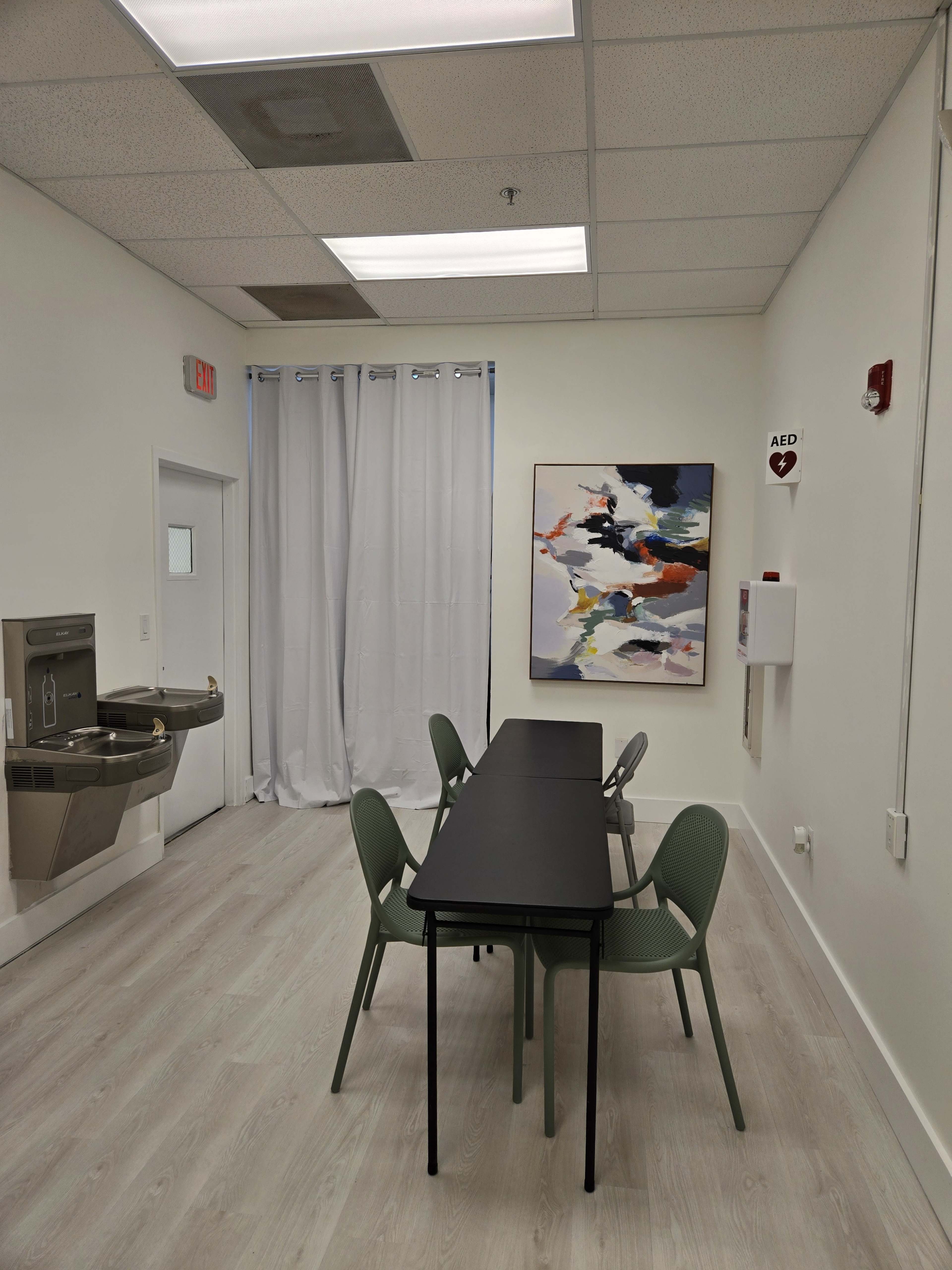 The room features a table with four chairs, a water fountain, and a large abstract painting on the wall.