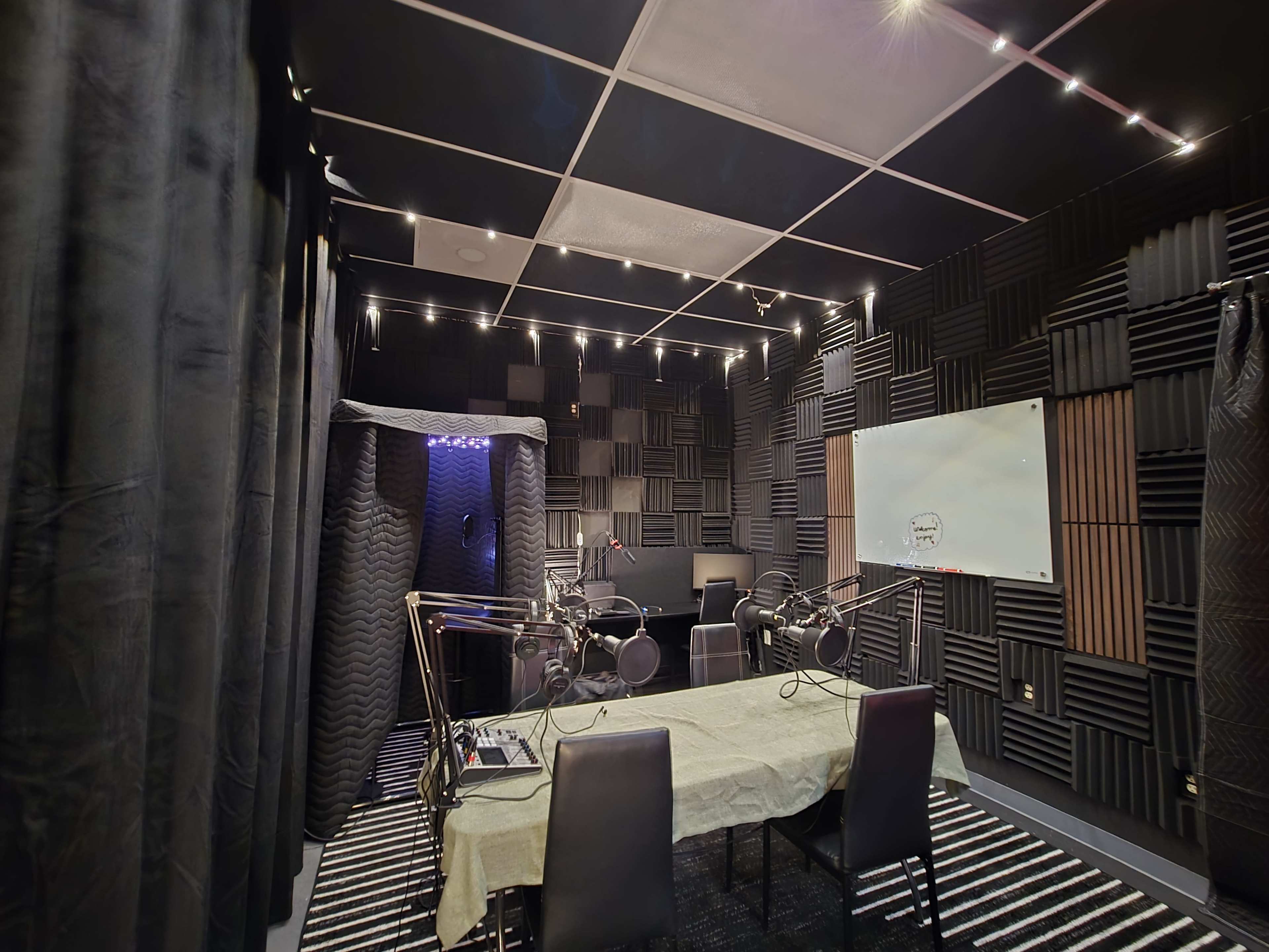The image shows a soundproof recording studio featuring a table with chairs, audio equipment, microphones, and acoustic wall panels.
