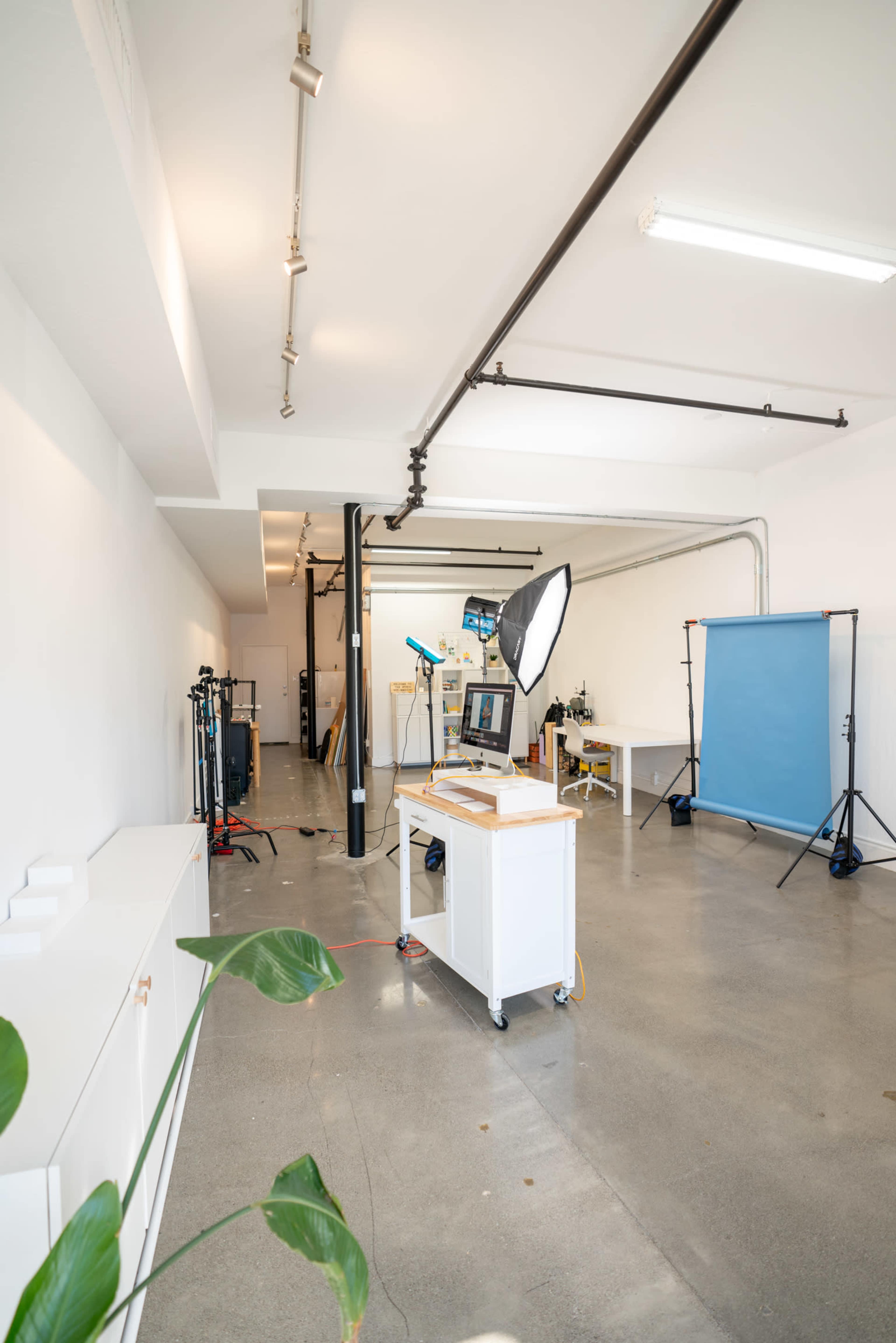 A spacious, well-lit studio with a blue backdrop, lighting equipment, and a workstation on wheels.