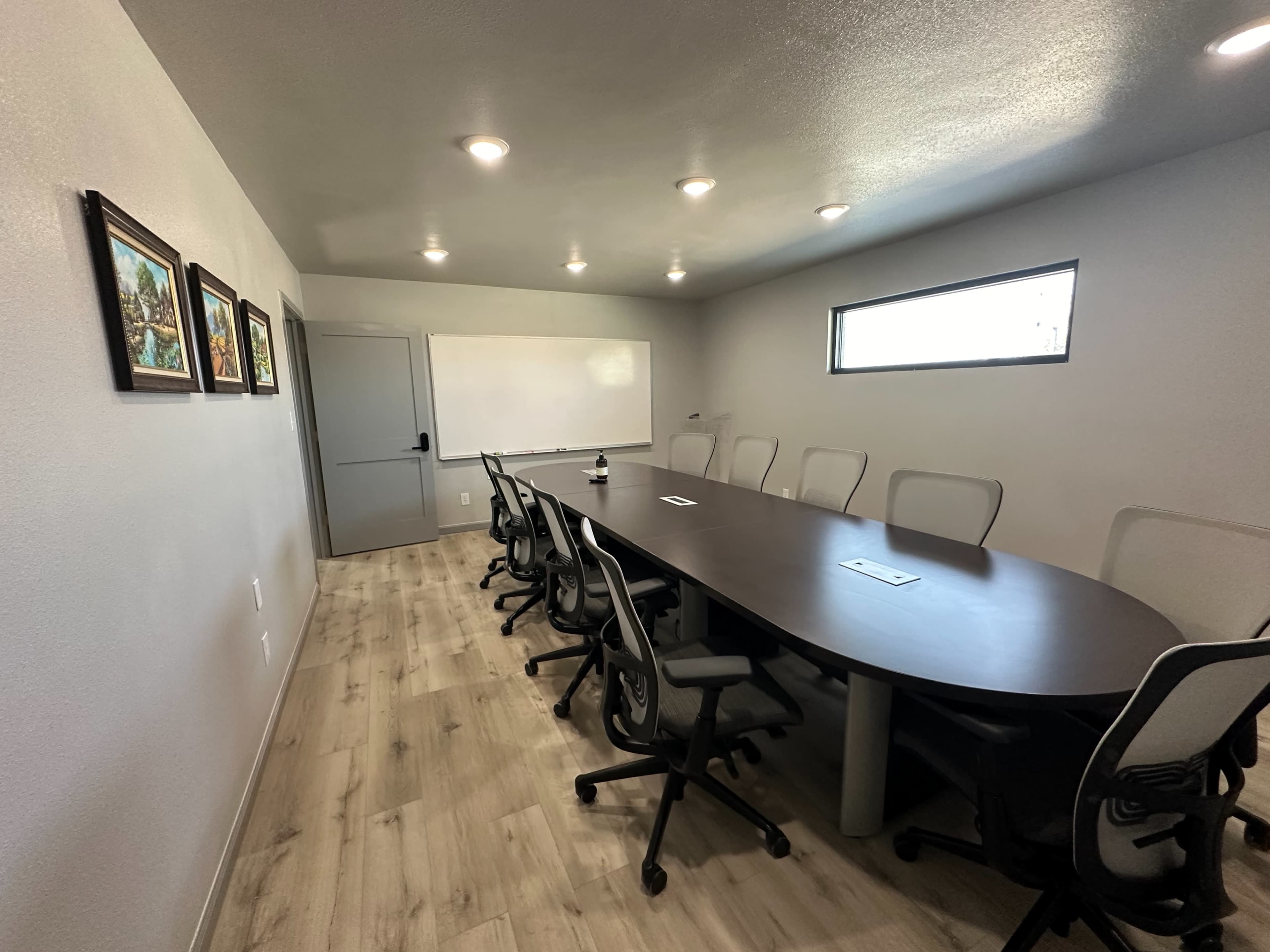 The image shows a modern conference room with an oval table surrounded by ergonomic chairs and framed artwork on the walls.