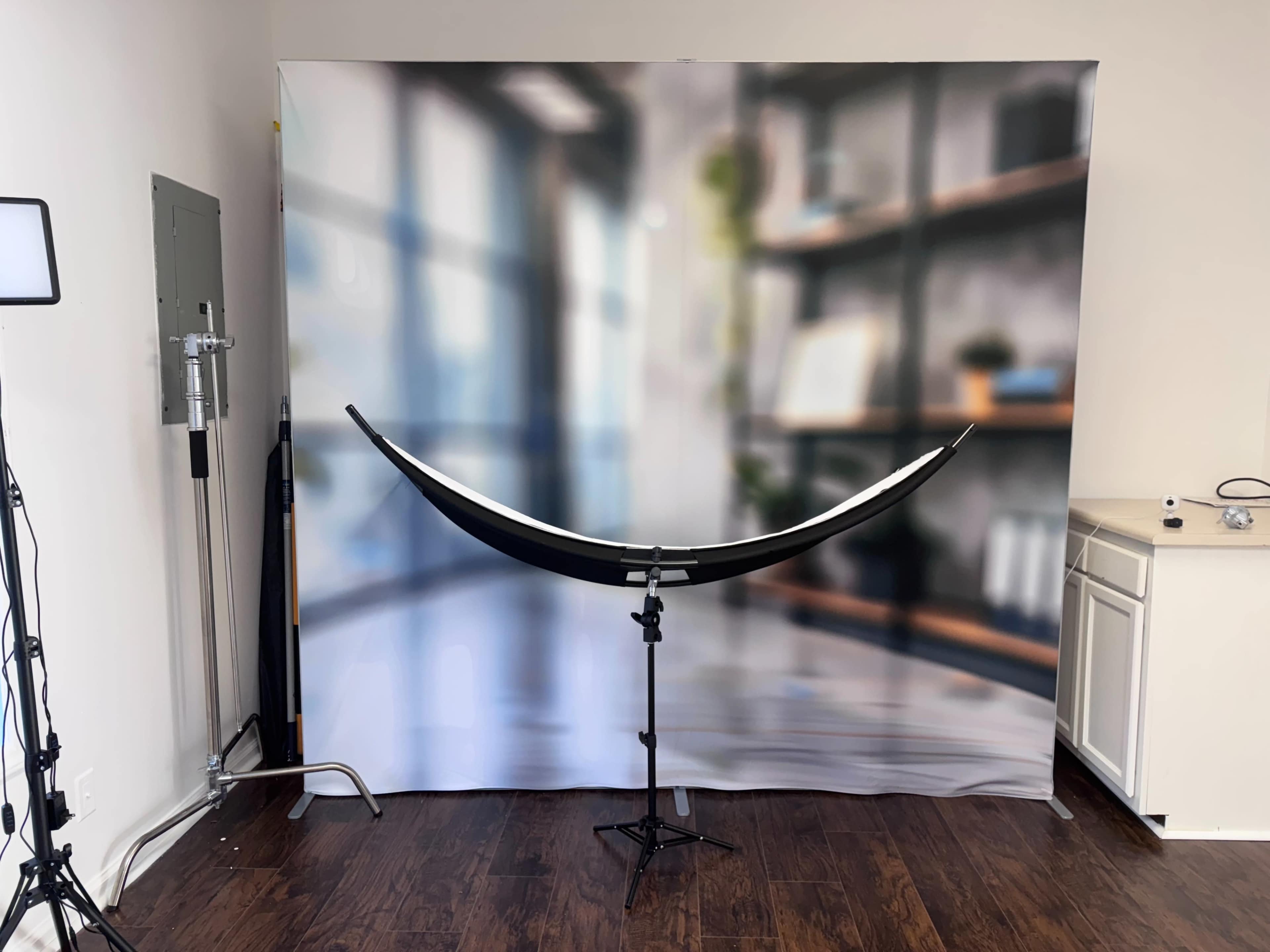 The image shows a photography setup with a curved backdrop stand and a blurred interior scene of shelves and windows in the background.
