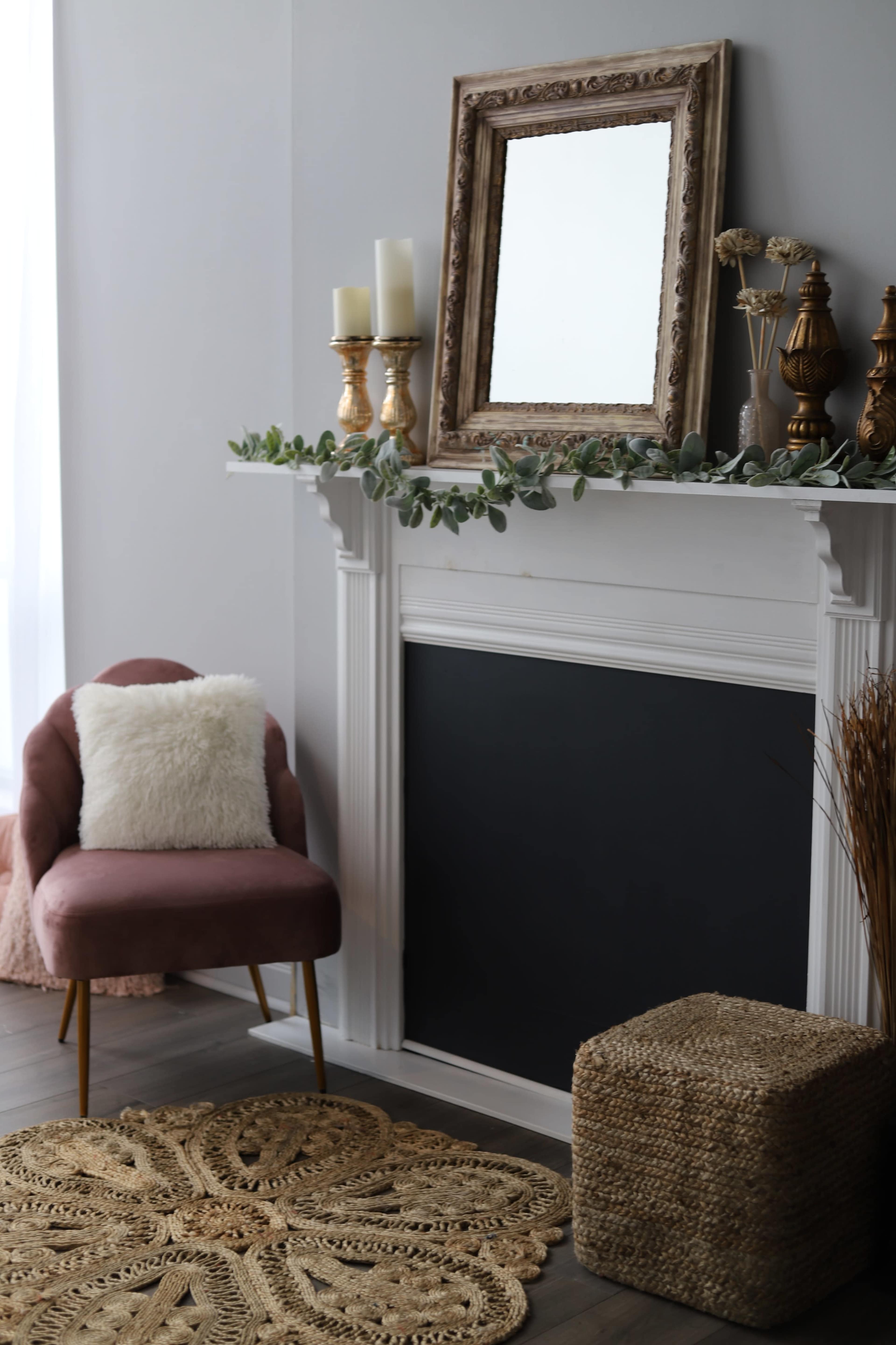 A cozy living room features a decorative fireplace with a mirror and candles, accompanied by a pink chair and a woven basket.