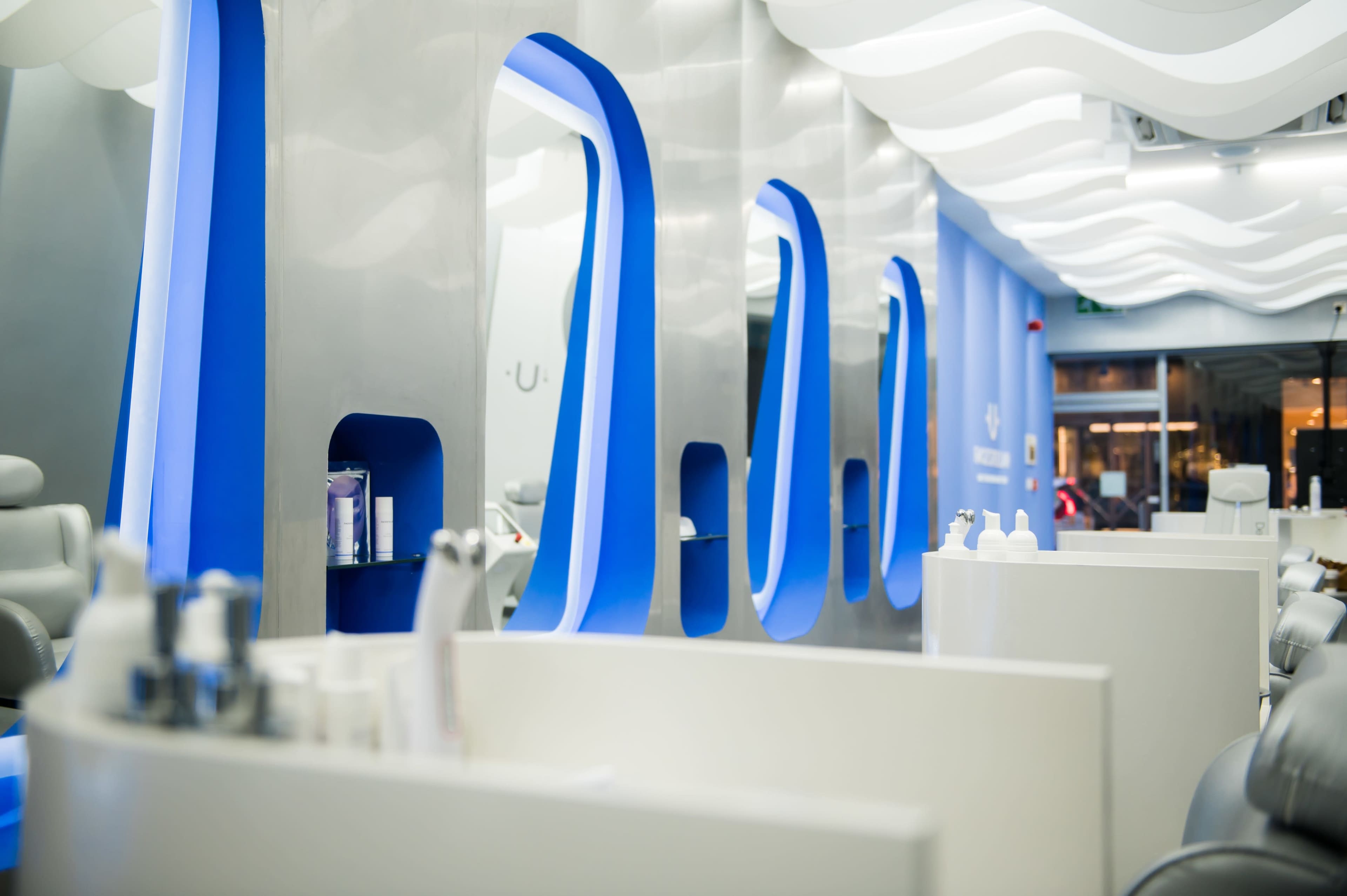 A modern salon interior with sleek blue and white design elements, featuring curved mirrors and workstations.