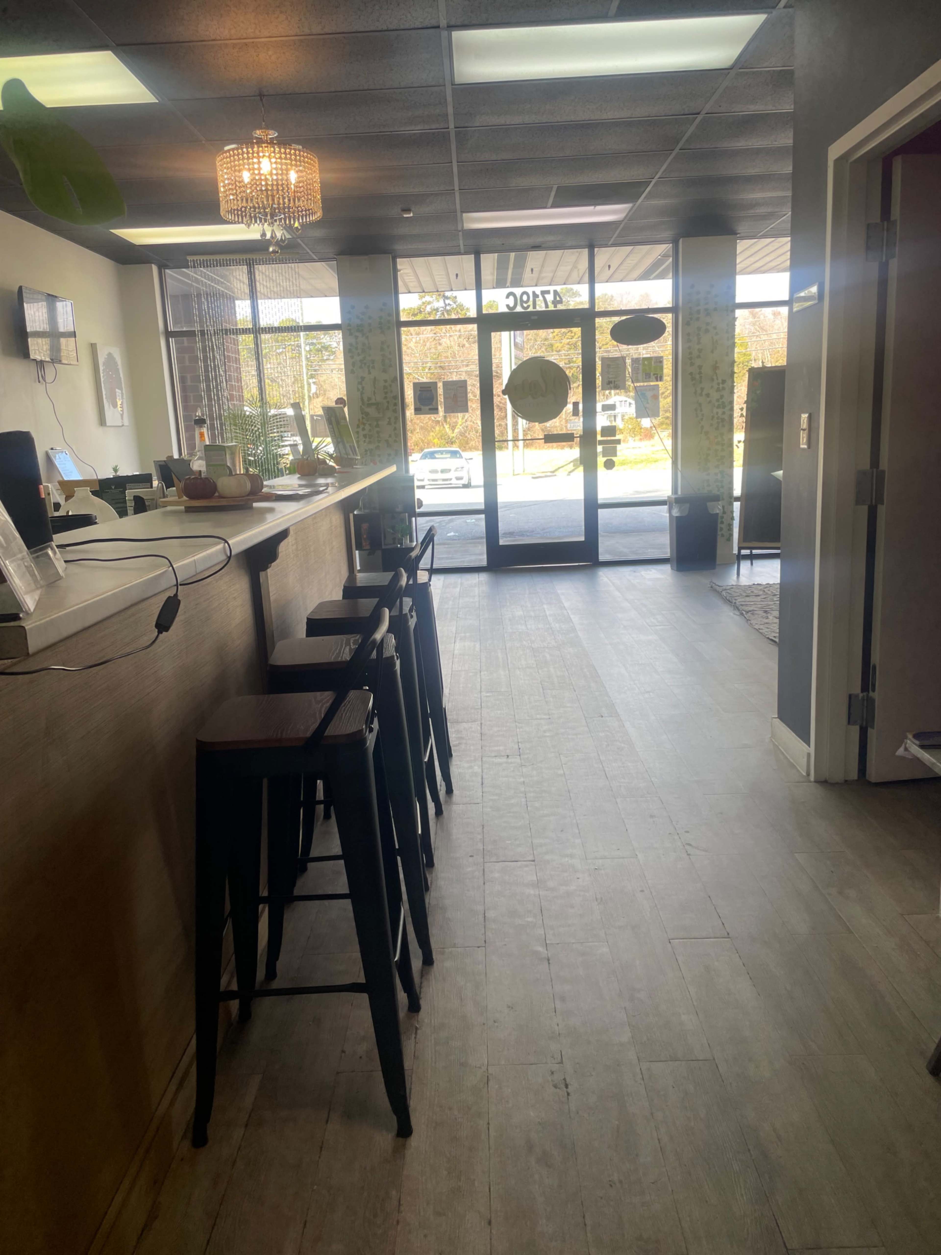 The image shows a modern interior of a cafe or reception area with a long counter and several high chairs facing the entrance.