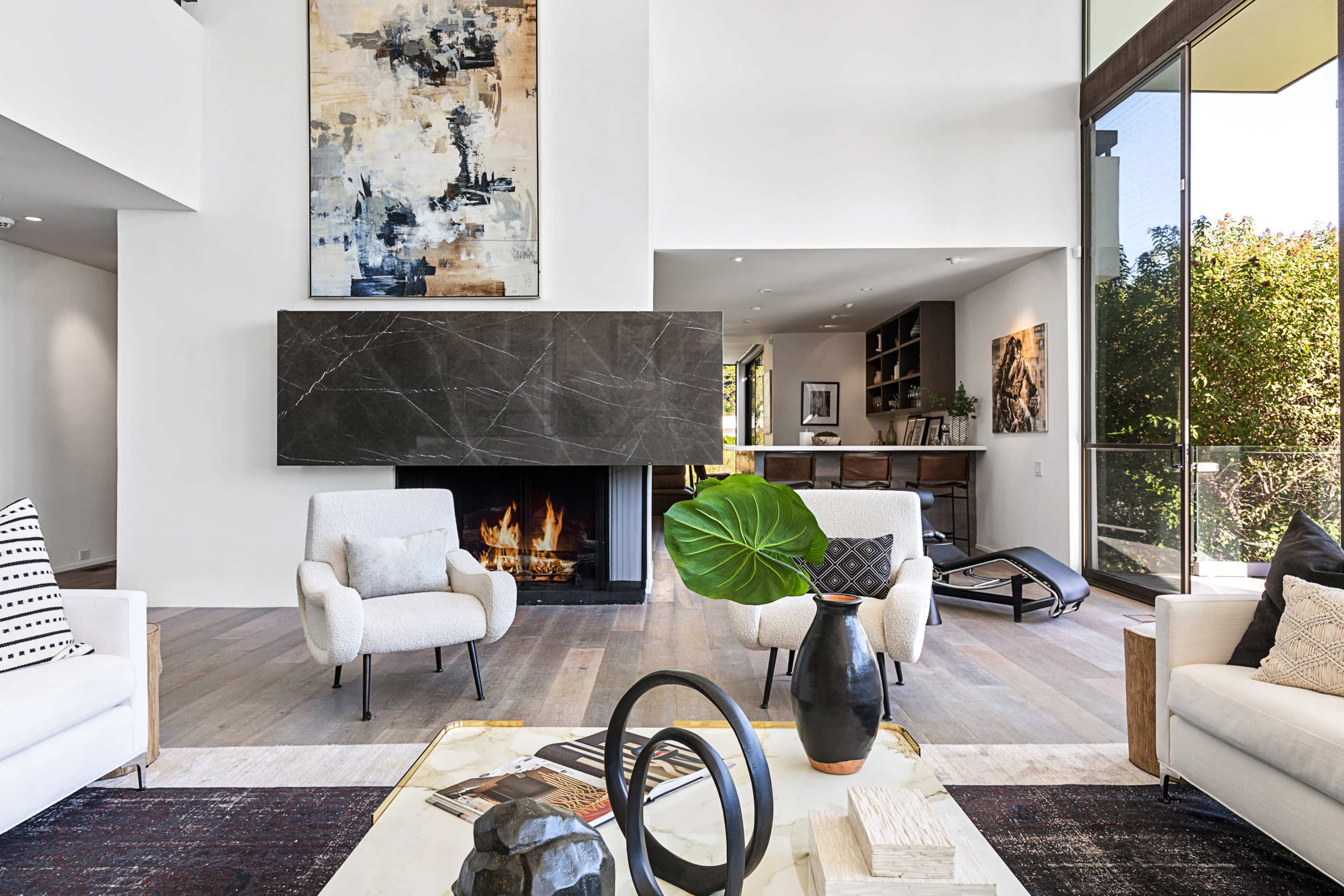 A modern living room with a minimalist design, showcasing a fireplace, large windows, and stylish furniture.