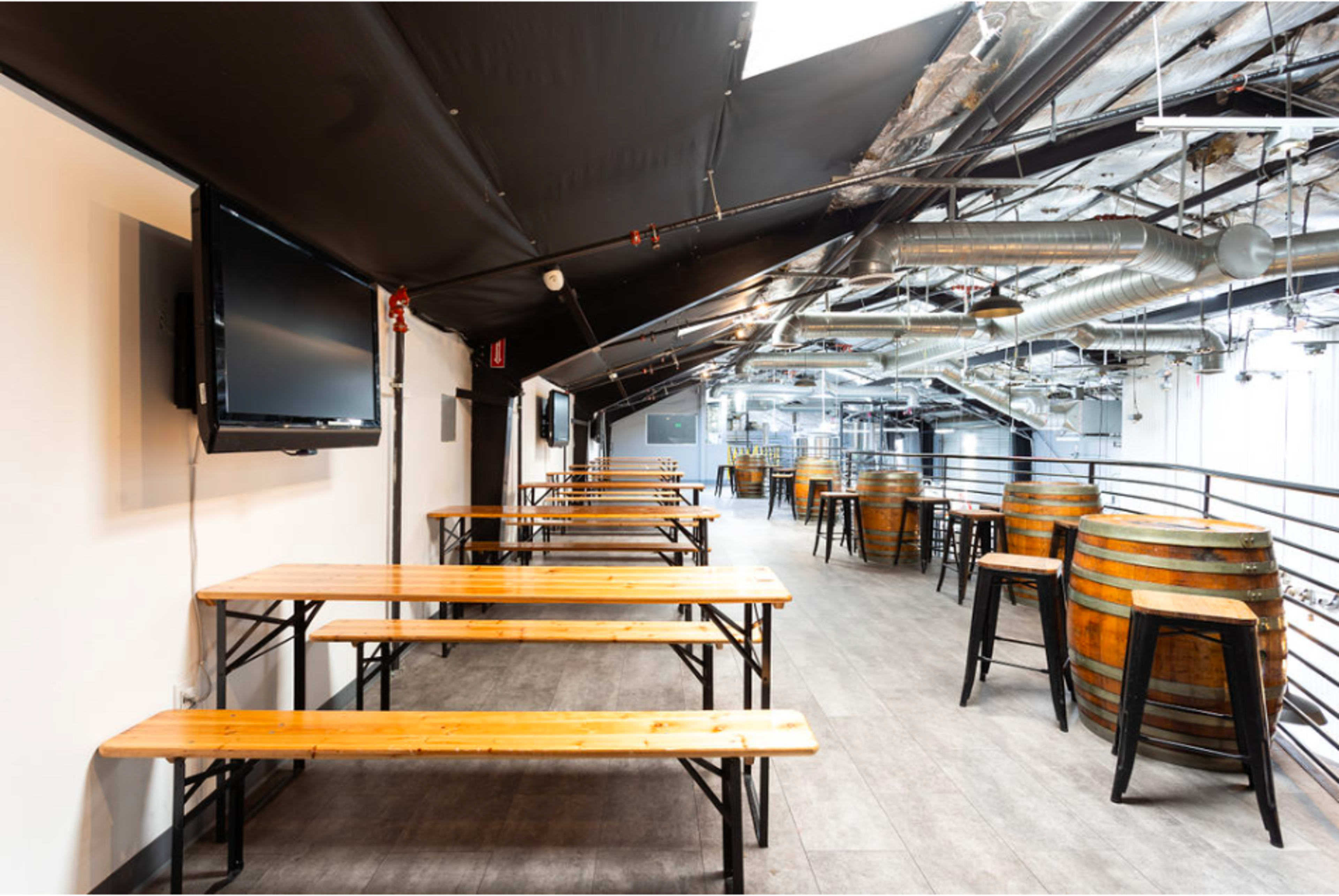 A spacious, industrial-style venue with wooden tables and barrels arranged in a bright, well-lit area.