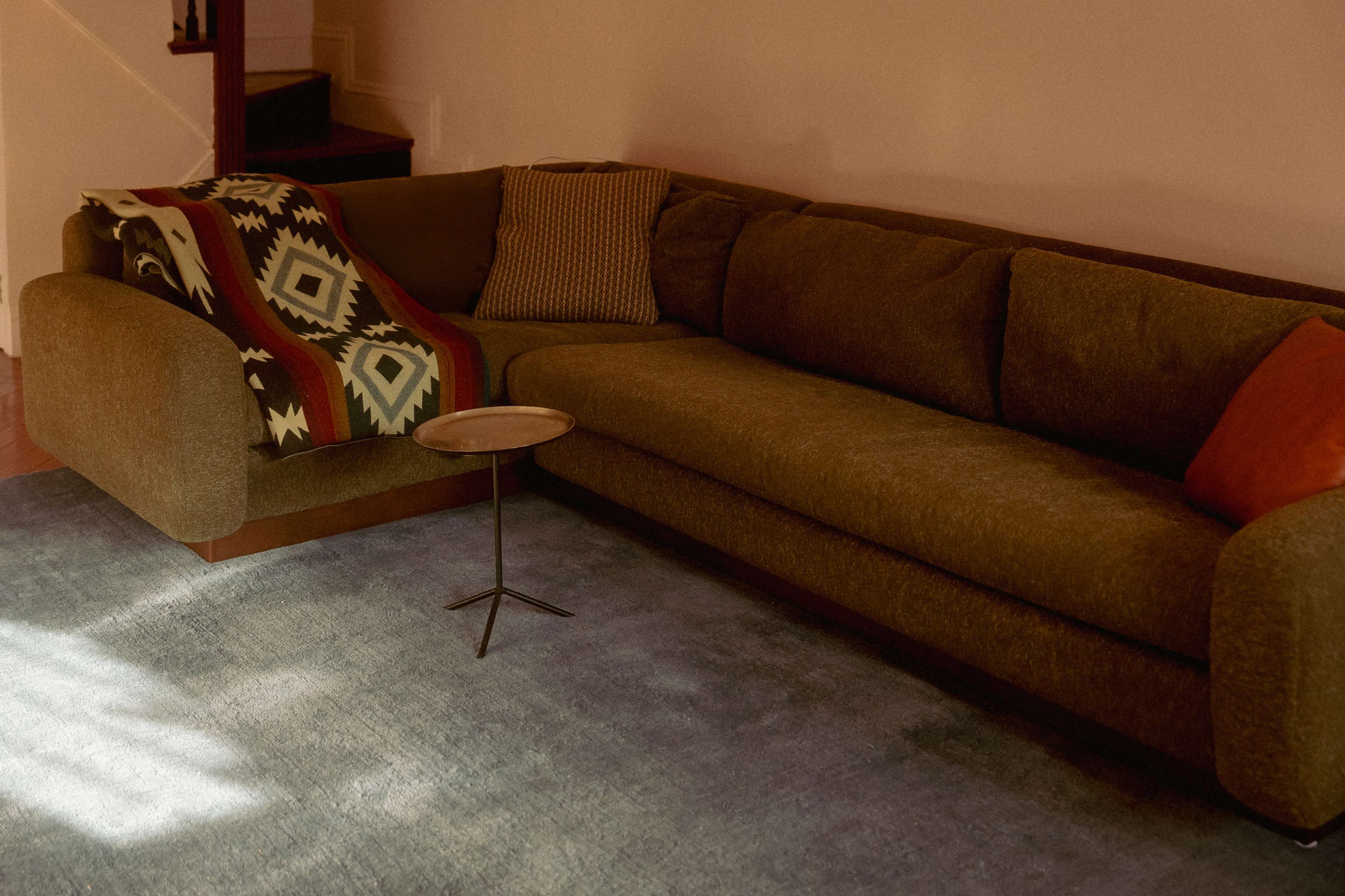 A large, textured sofa with a patterned blanket rests on a blue area rug, complemented by a small side table nearby.
