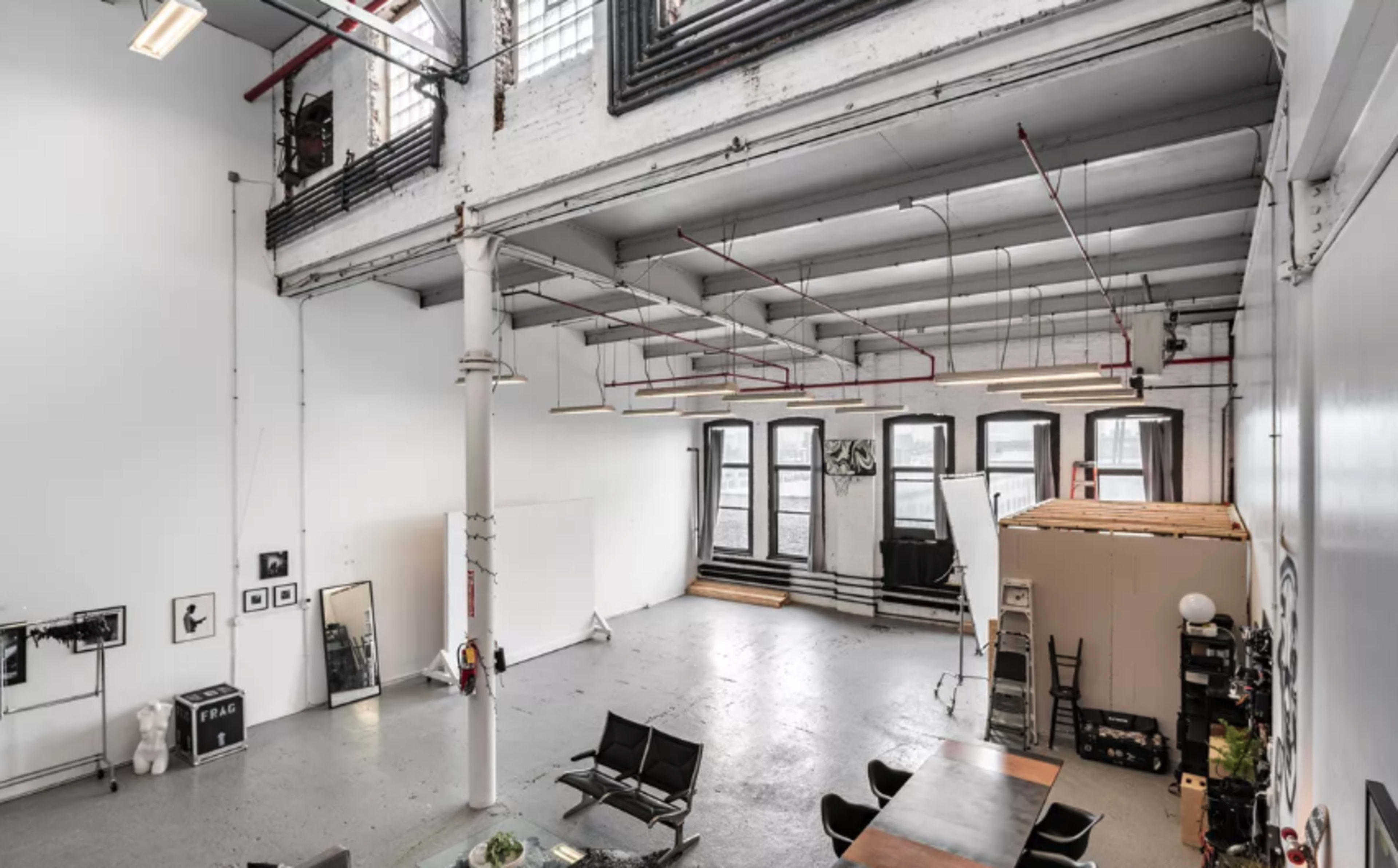A spacious, open loft with high ceilings, large windows, and industrial-style elements, featuring a dining table and various furnishings.