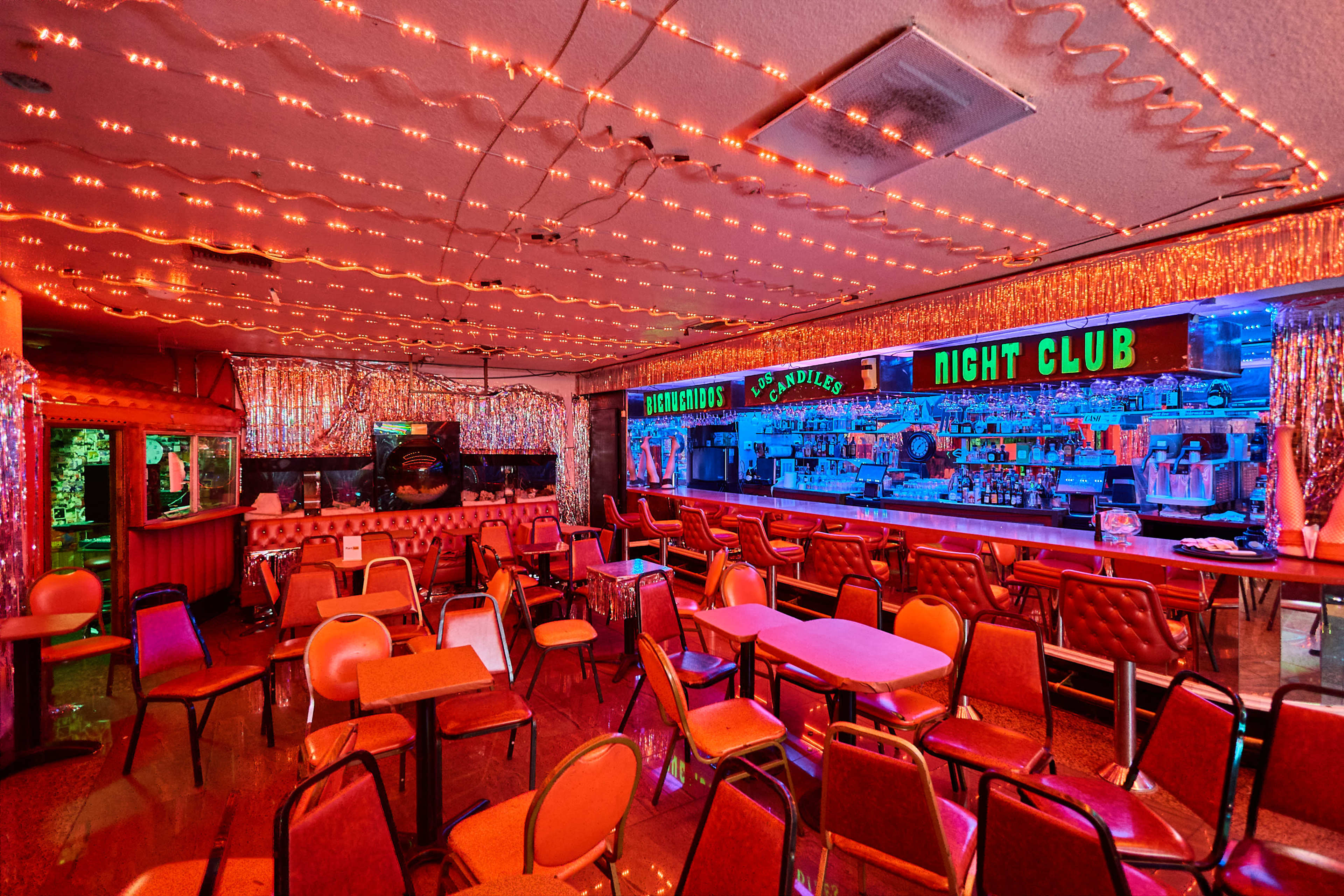 The image shows an empty nightclub interior adorned with colorful lights and a bar area in the background.