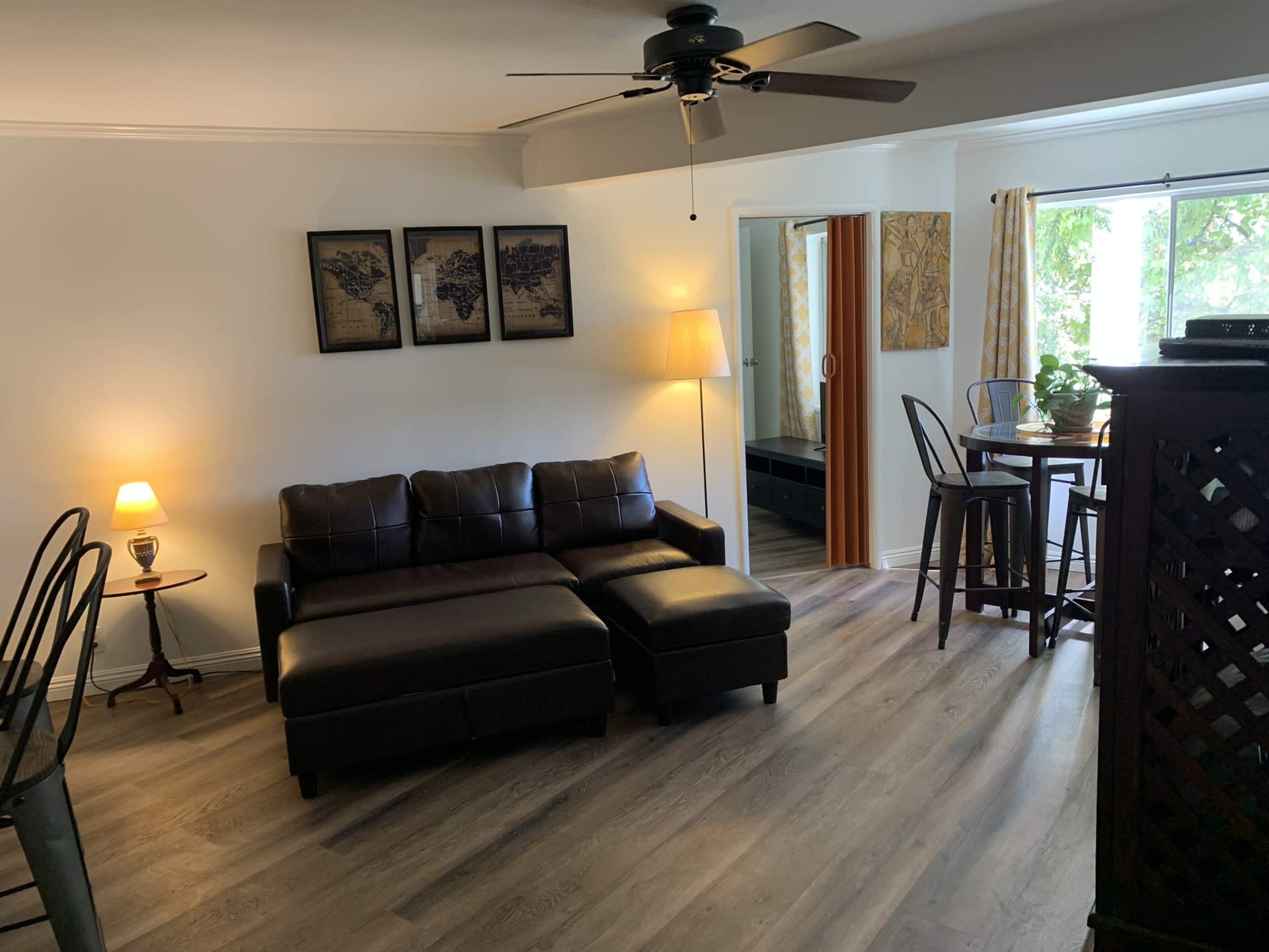 A modern living space with a dark brown sectional sofa, a small dining table, and a floor lamp, all set against light-colored walls and wooden flooring.