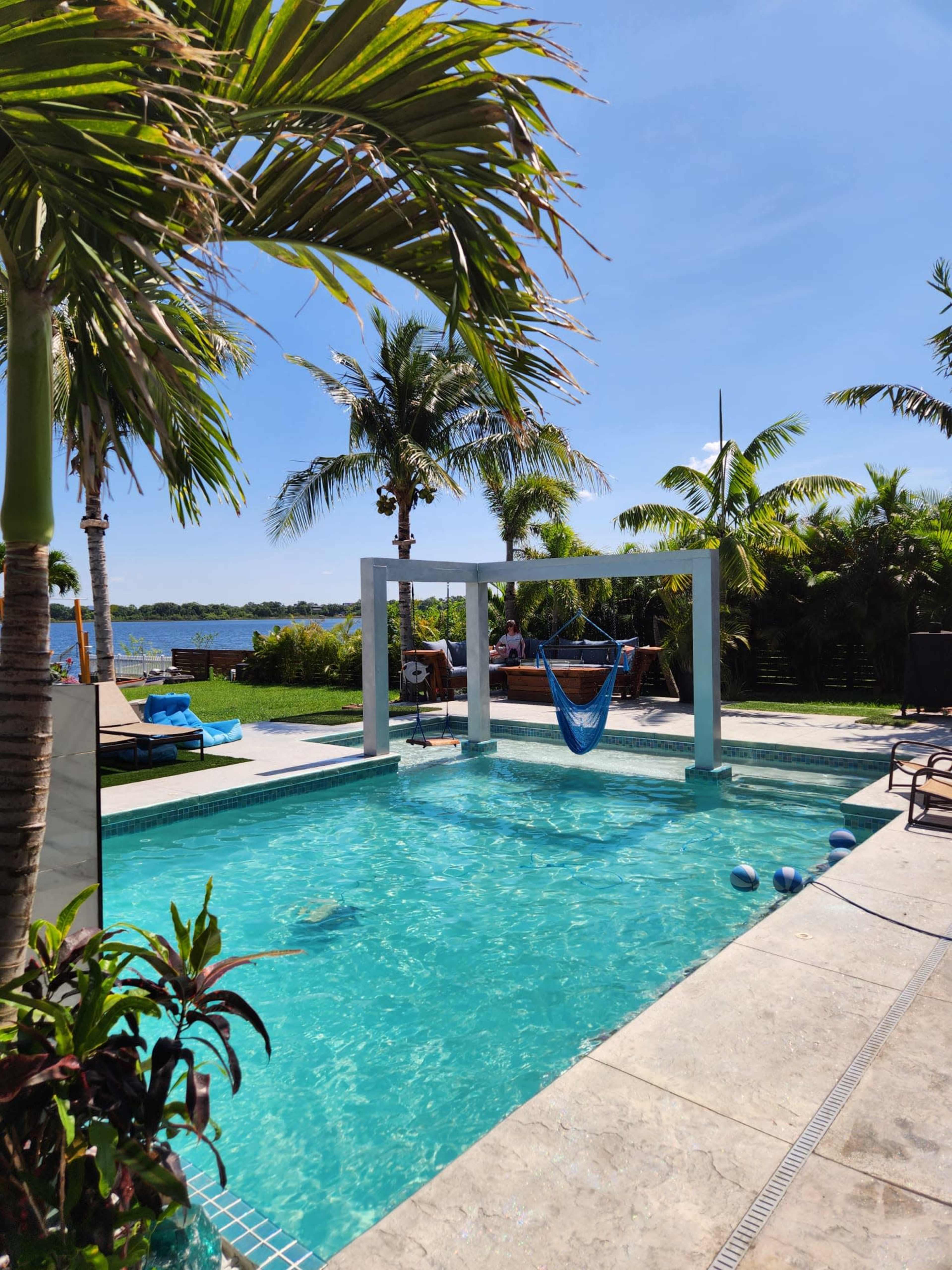 A swimming pool surrounded by palm trees and a hammock, with a scenic view in the background.