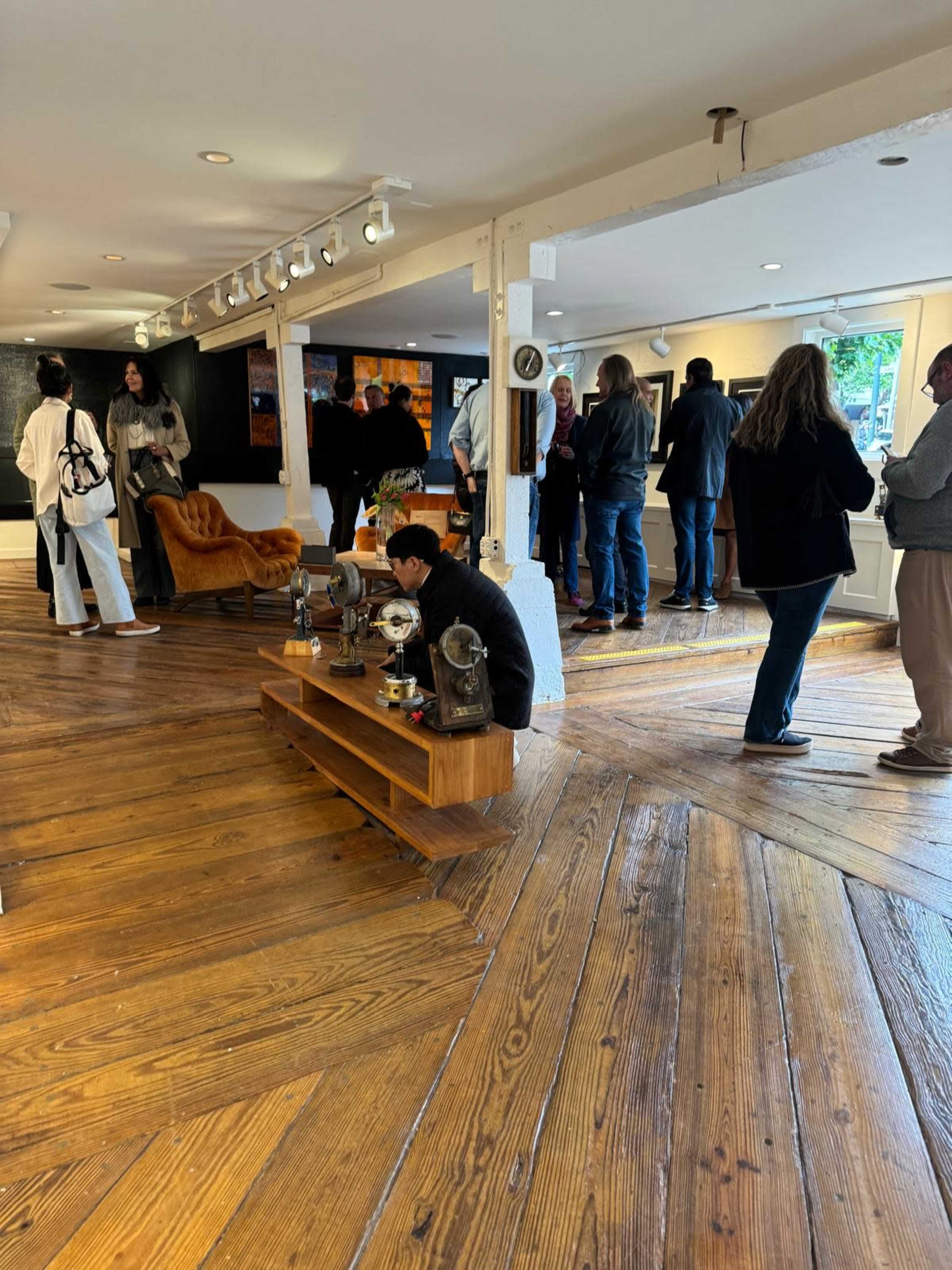 A group of people attends an event in a modern gallery with wooden floors and a mix of seating arrangements.