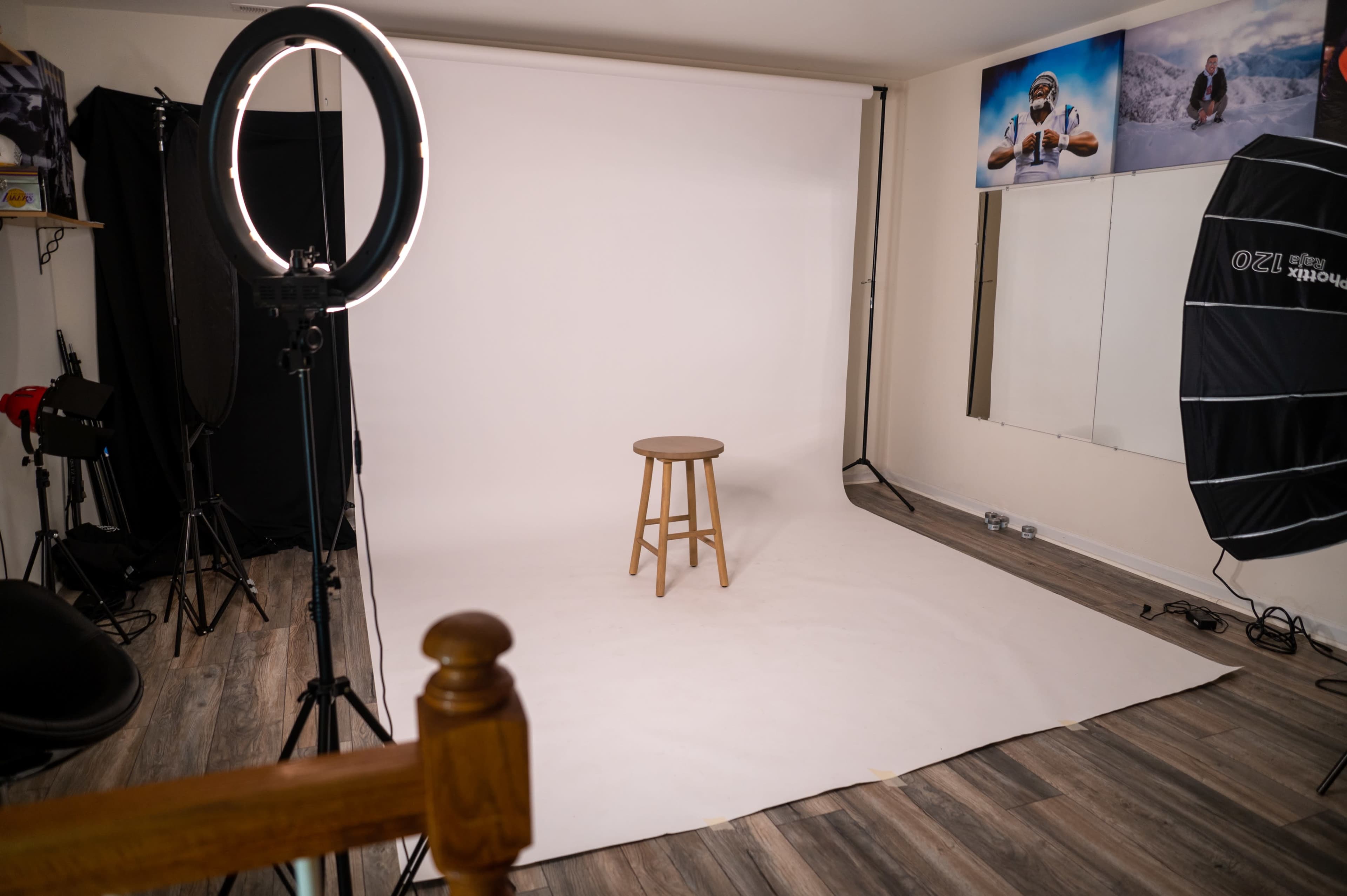 A photography studio with a stool on a plain white backdrop, surrounded by softbox lighting and a ring light.