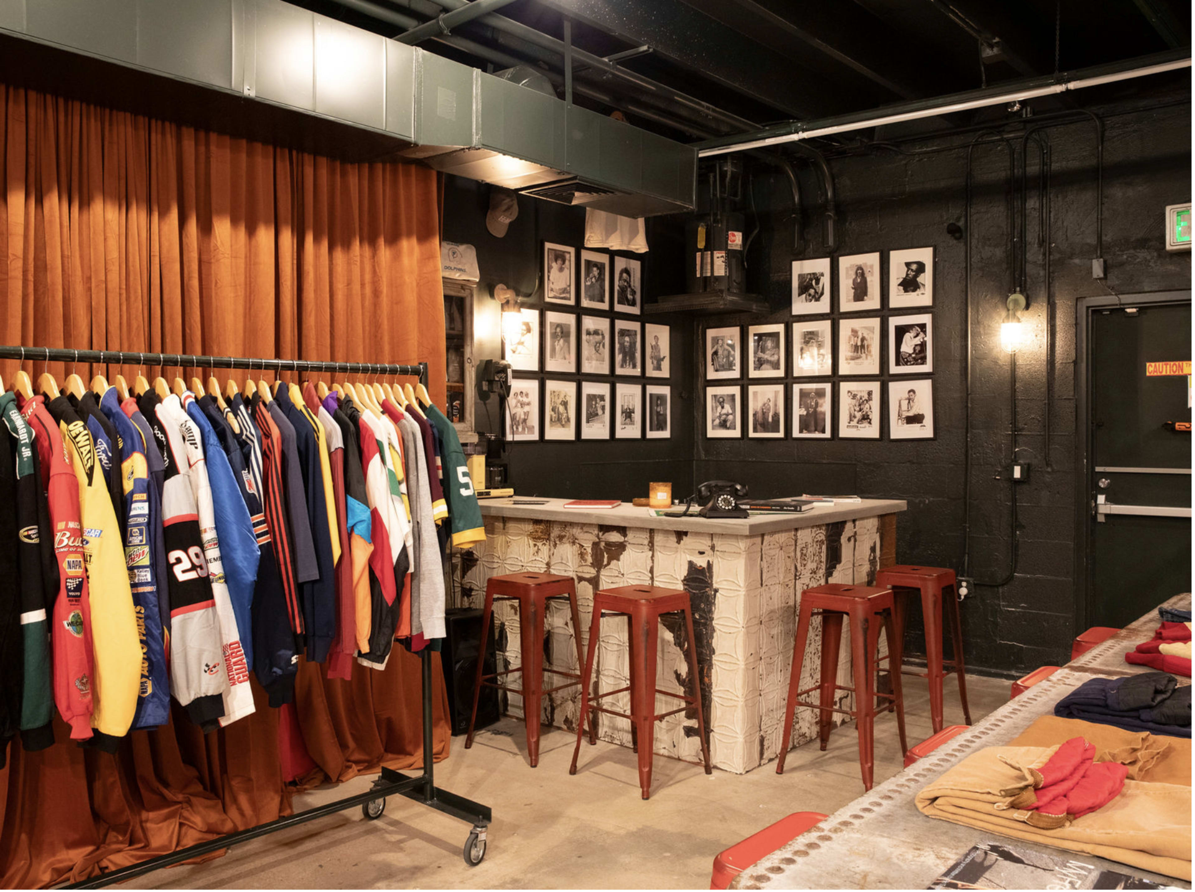 The image shows a room with a bar area and a clothing rack displaying colorful jerseys, alongside a wall adorned with framed black-and-white photographs.