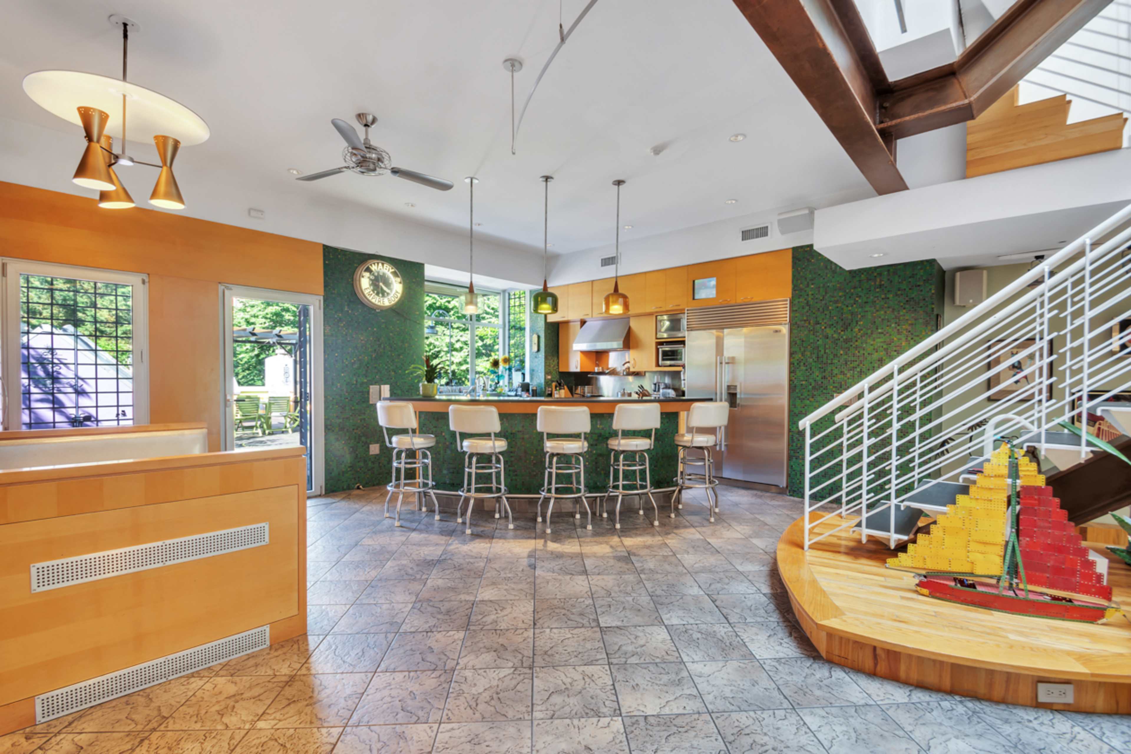 A modern kitchen and dining area with a circular bar, stainless steel appliances, and a staircase featuring wooden steps.
