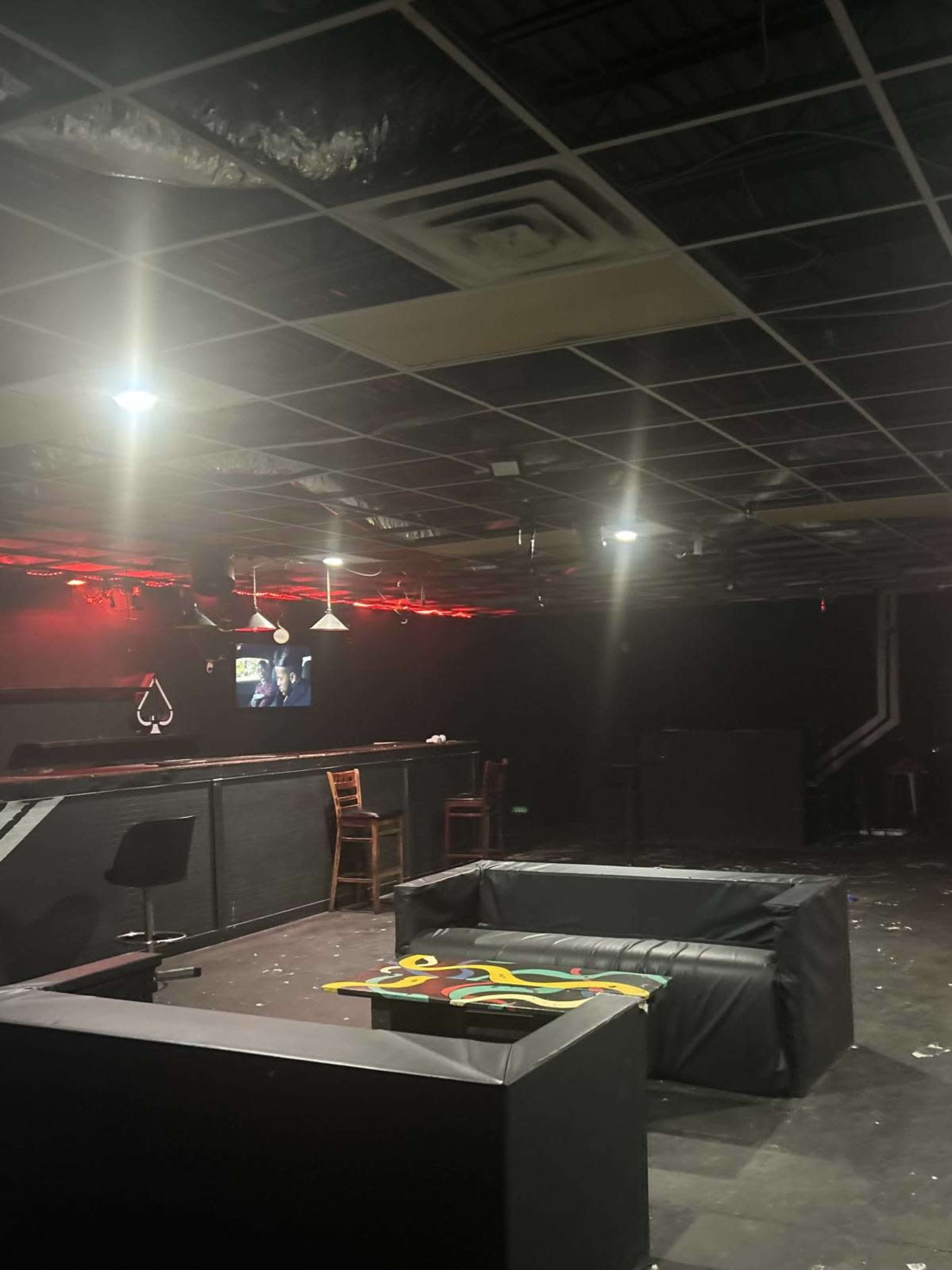 A dimly lit lounge area features a black couch, a bar with chairs, and a TV screen against a dark backdrop.