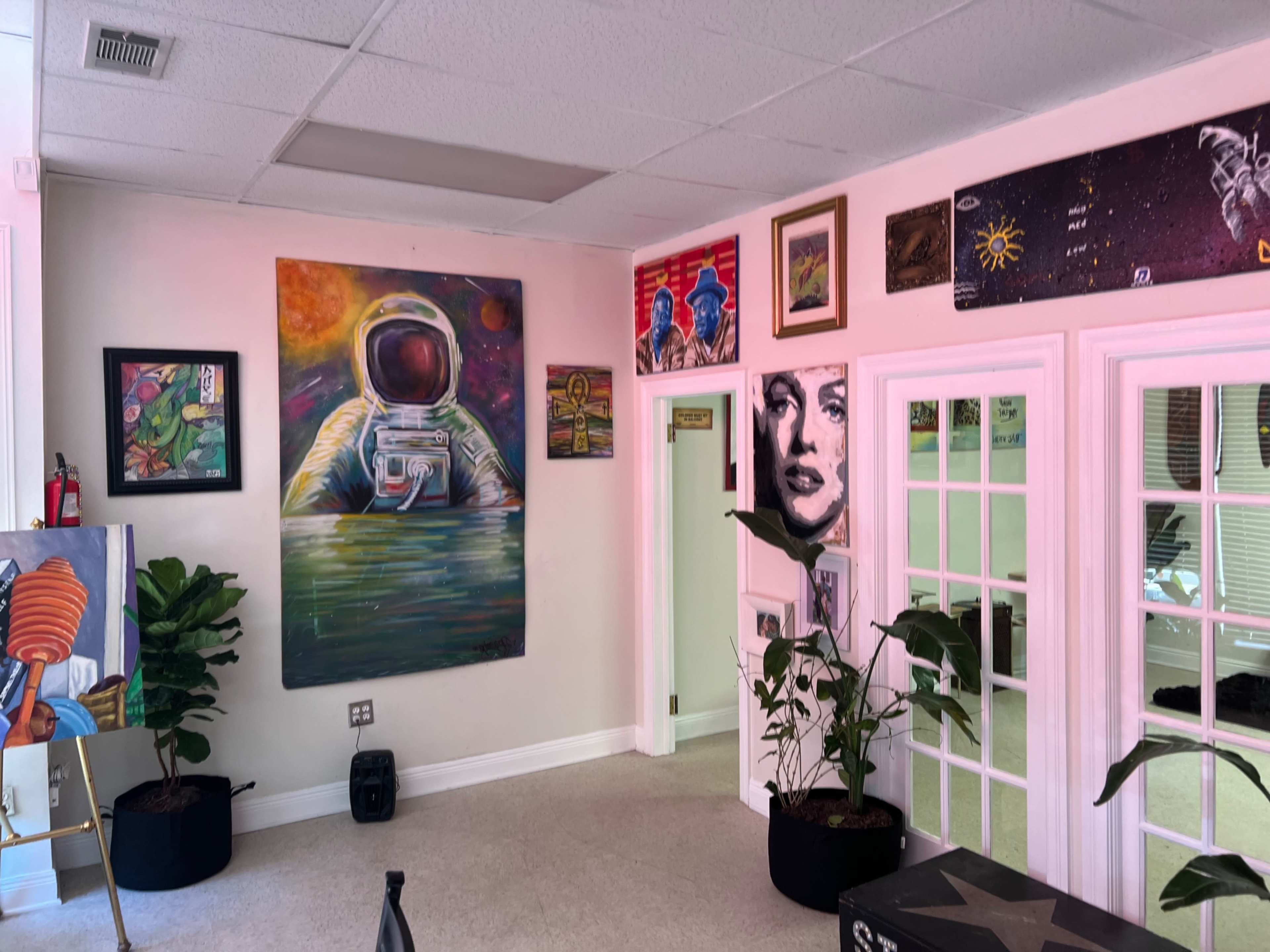 The room features a large astronaut mural, several framed paintings on the walls, and indoor plants in black pots.