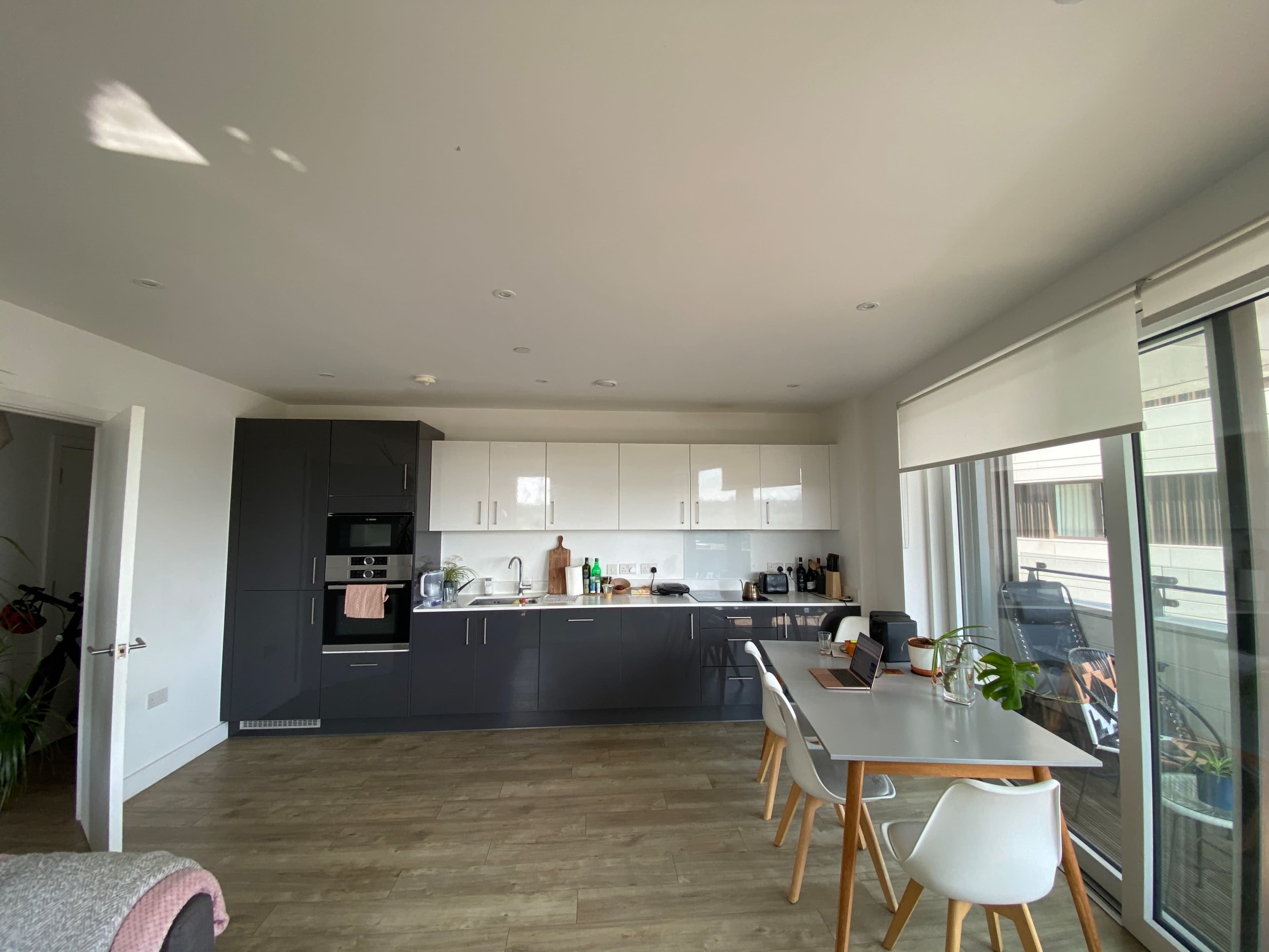 A modern kitchen with gray and white cabinetry, featuring stainless steel appliances and a dining table set near a large window.