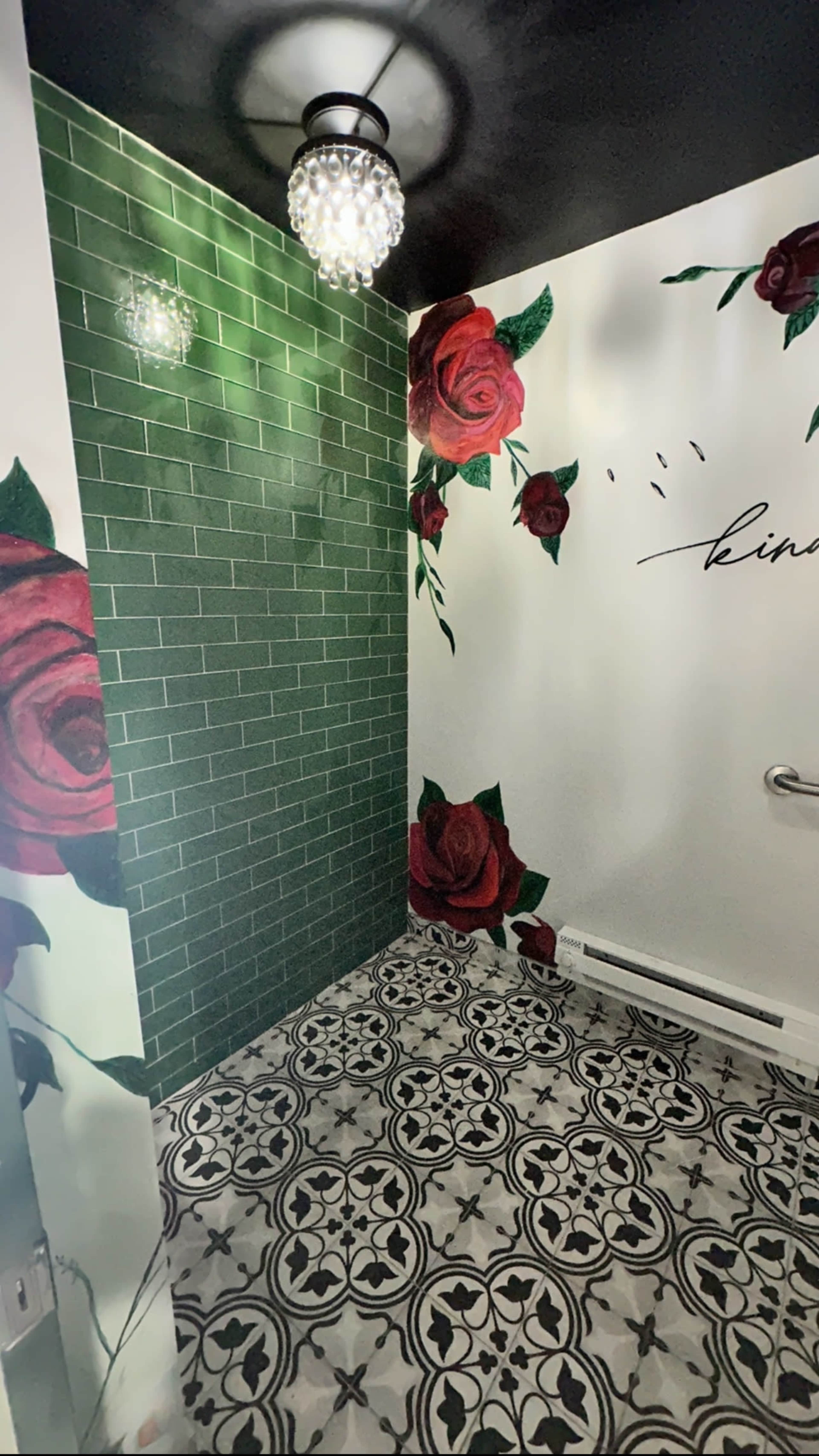 A bathroom with green tiled walls adorned with large rose murals and a patterned black and white floor.