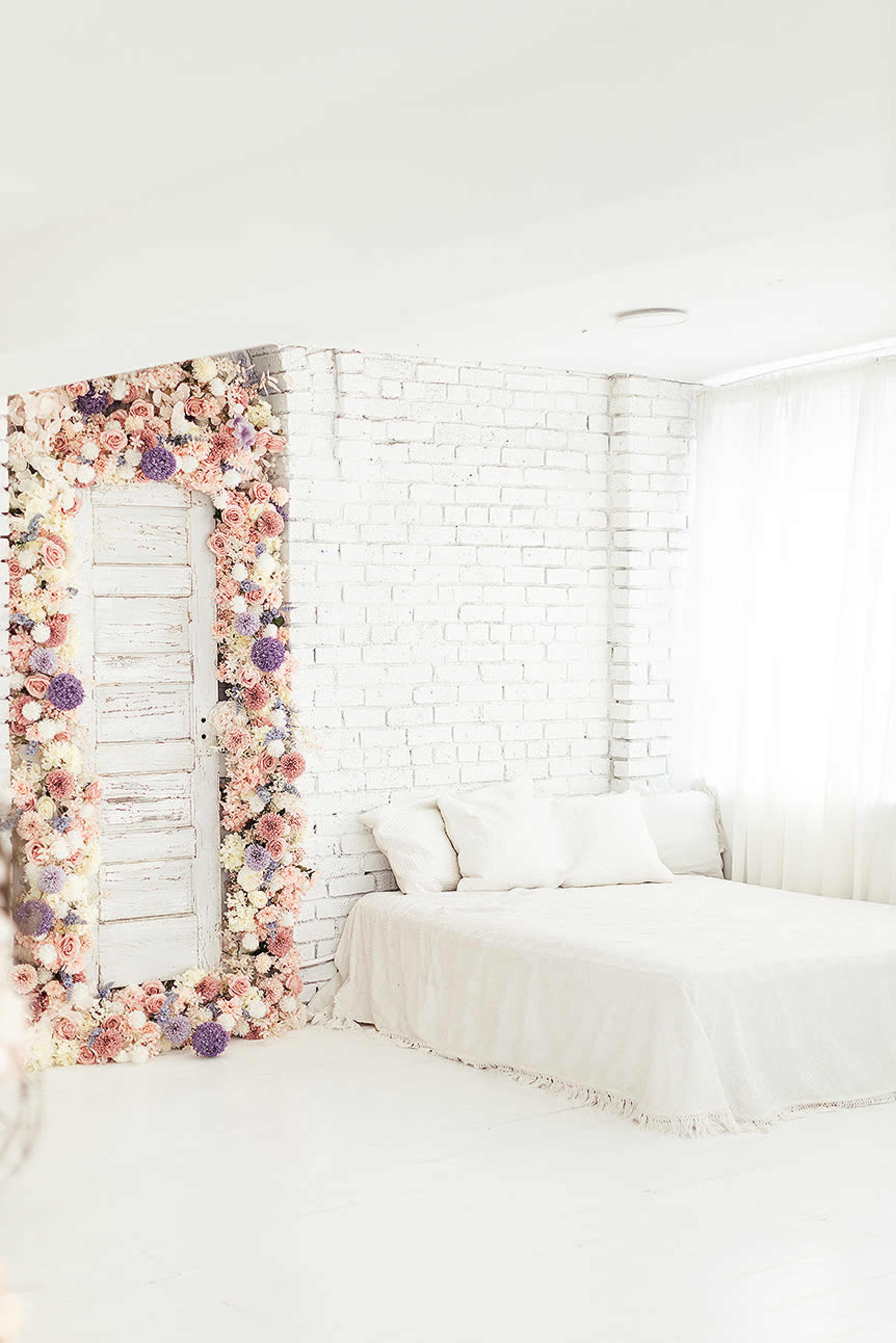 A minimalist bedroom features a bed and a decorative floral frame around a white wooden door against a brick wall.