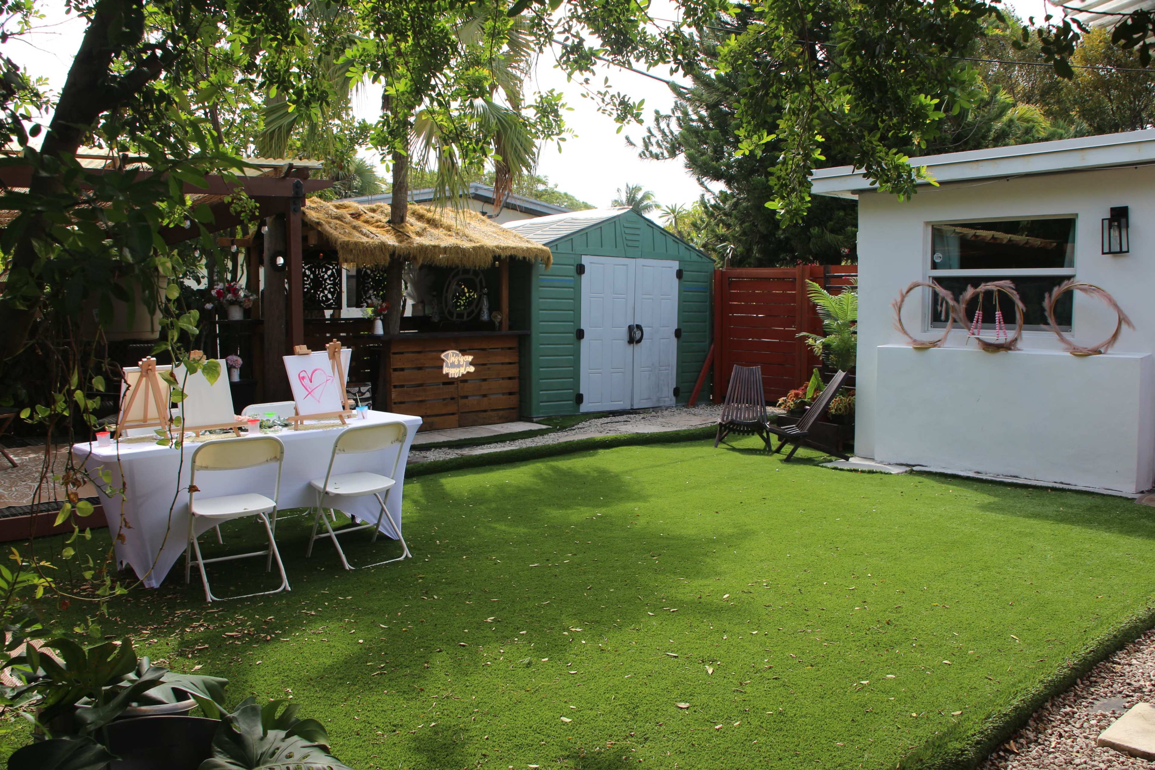 A well-maintained backyard features a table set for an event, surrounded by greenery, with a shed and a gazebo visible in the background.