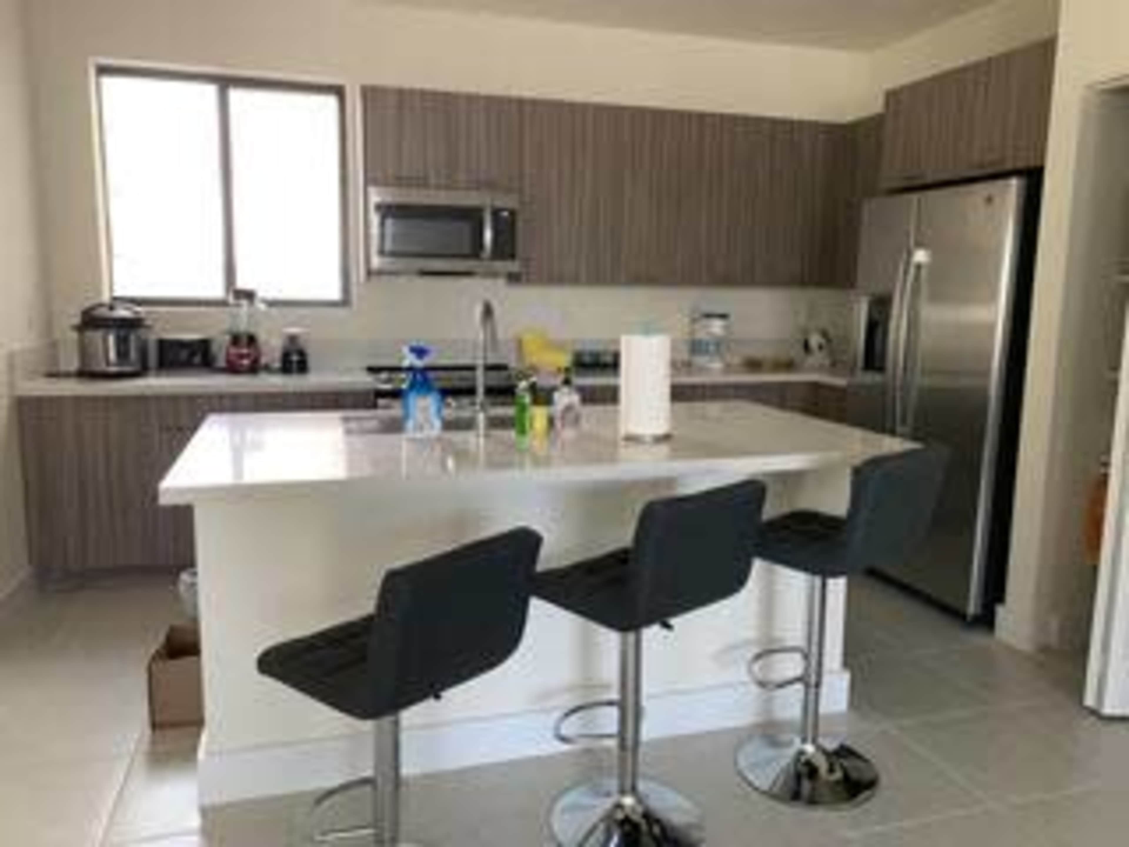 A modern kitchen features gray cabinetry, stainless steel appliances, and a central island with three black bar stools.