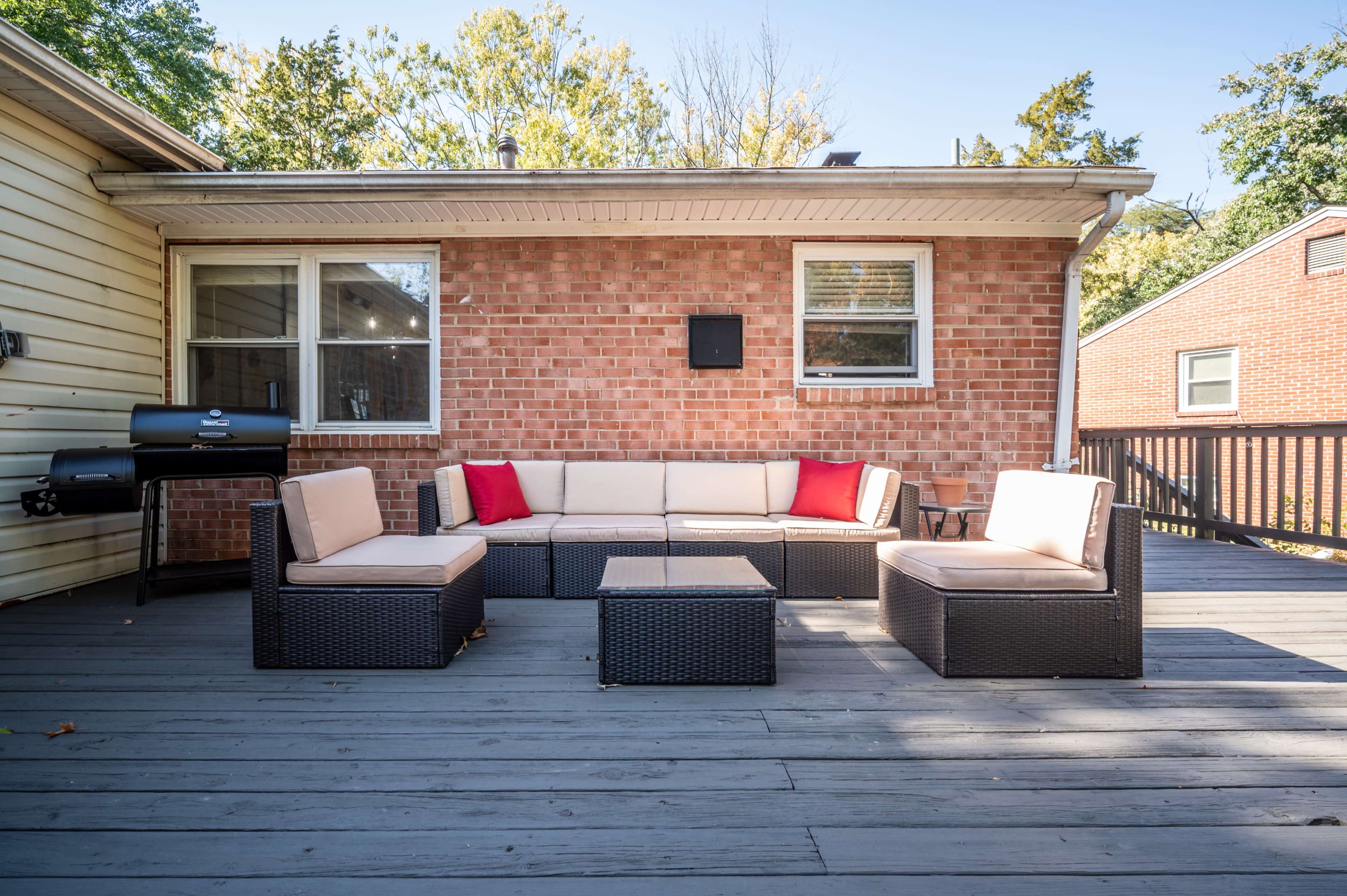 The image shows a patio with a seating arrangement consisting of a sectional sofa and a coffee table, set against a brick wall of a house.
