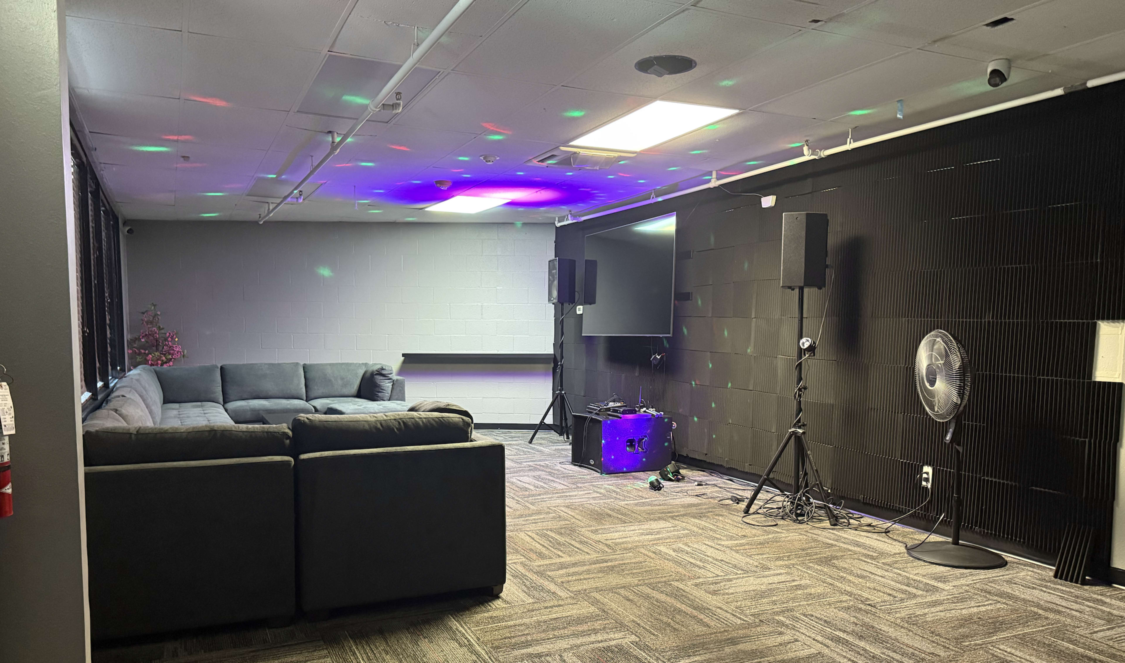The image shows a room with a sofa, a television, audio equipment, and a fan, featuring colorful lights projected on the ceiling.