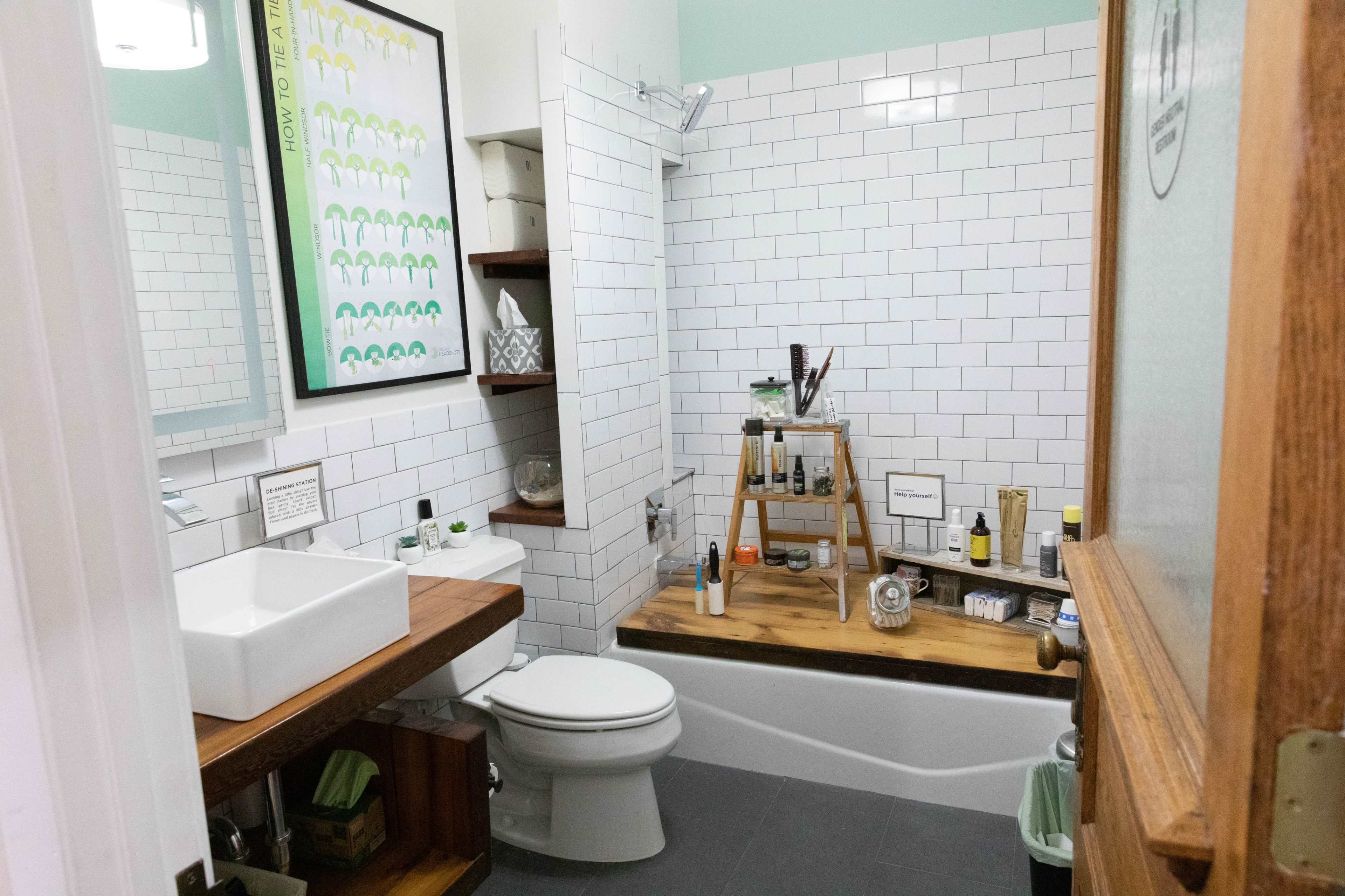 The image shows a bathroom featuring white subway tile walls, a wooden countertop with a square sink, and a bathtub with a wooden ledge displaying various toiletries.
